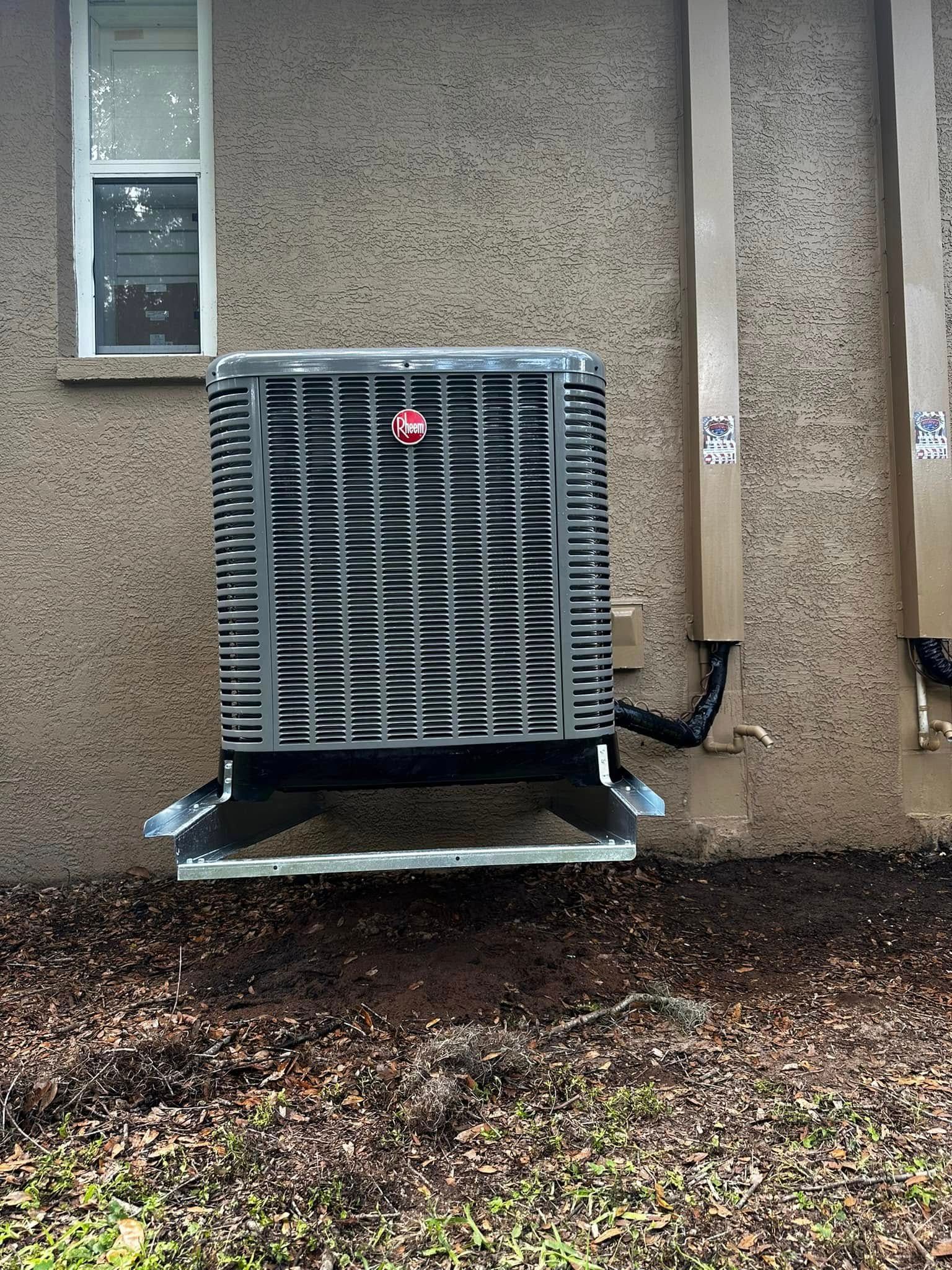 Outdoor HVAC unit mounted on a beige building wall above gravel and leaves