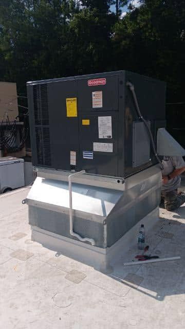 Large black HVAC unit on a white metal base outdoors in a paved area.