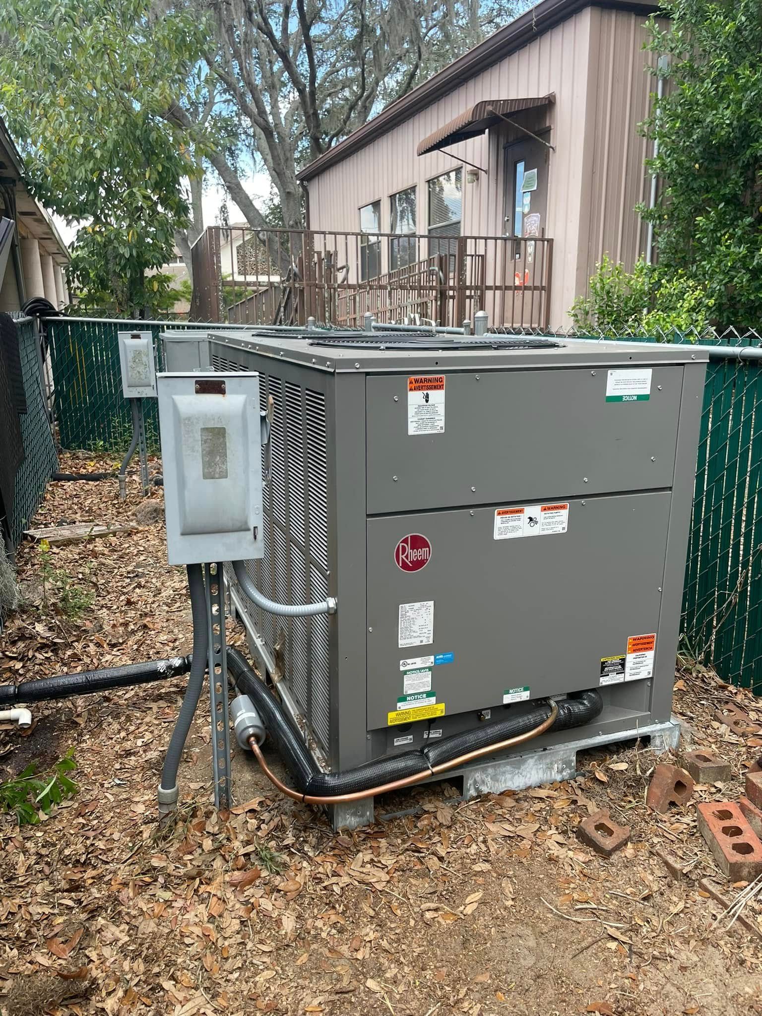 Gray electrical transformer with cables and a control box beside a house in a wooded yard