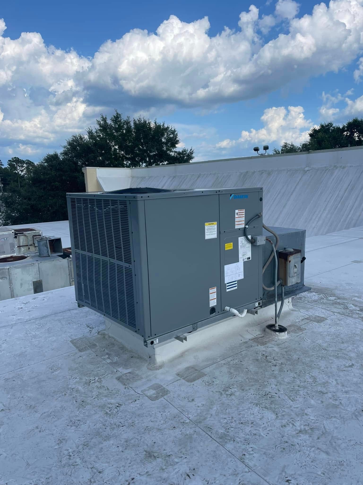 Gray rooftop HVAC unit on a flat white roof under a cloudy sky.