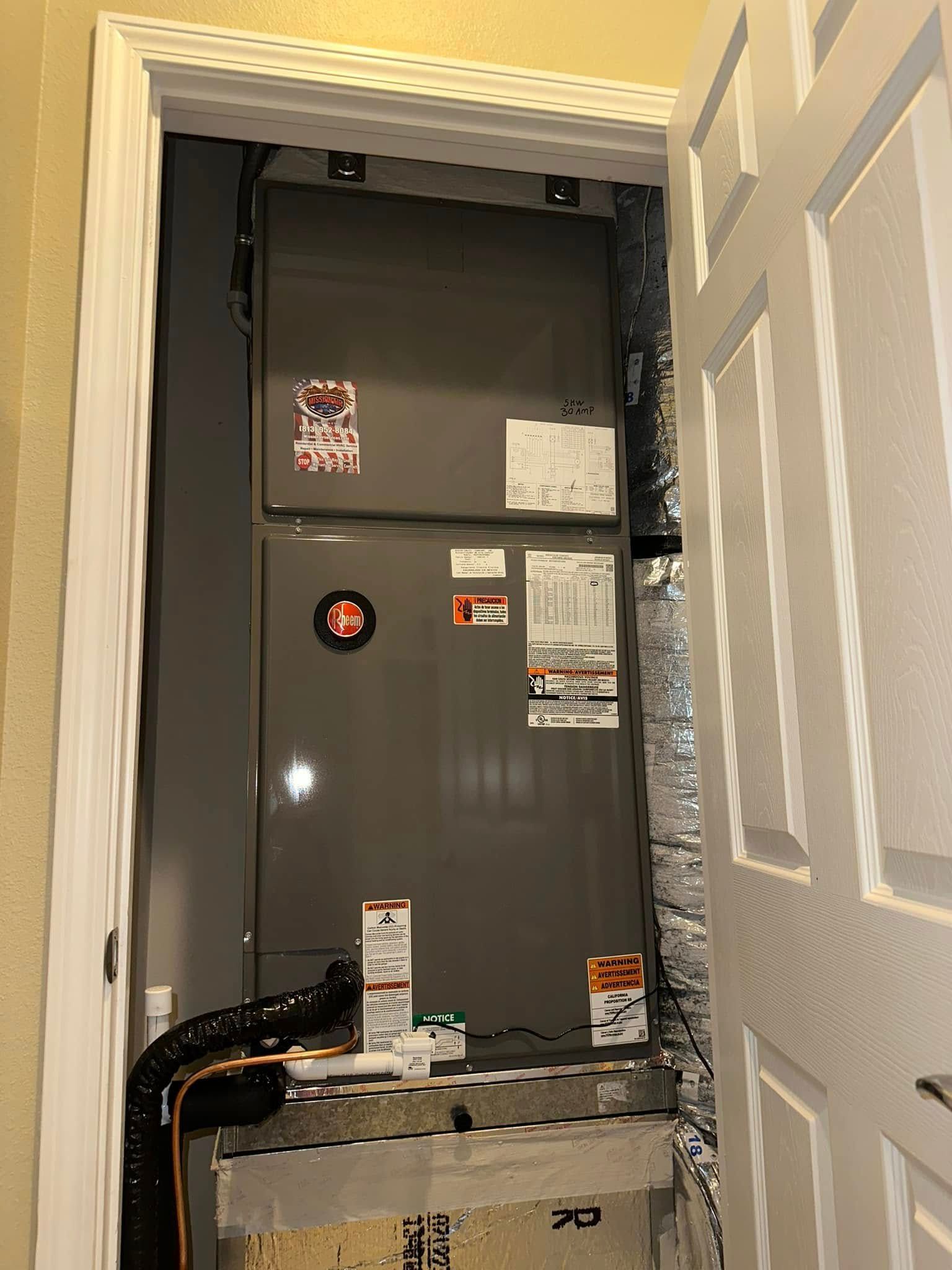 Open HVAC closet with gray furnace and exposed copper piping behind a white door