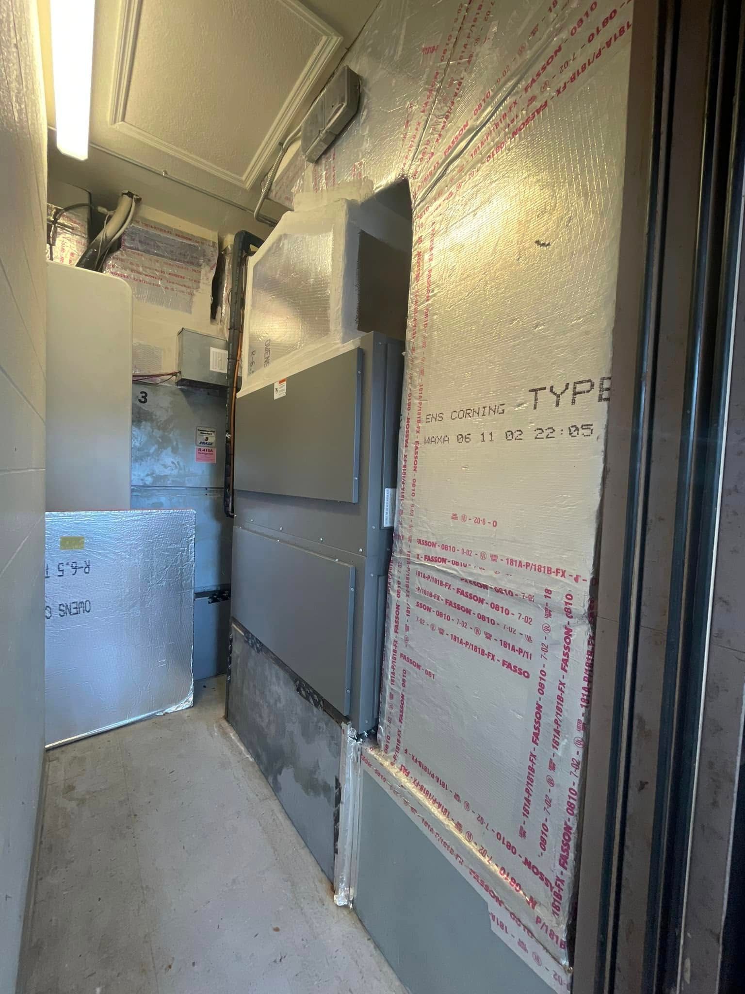 Narrow industrial hallway with metal panels, ductwork, and insulated wall sheathing under bright lights