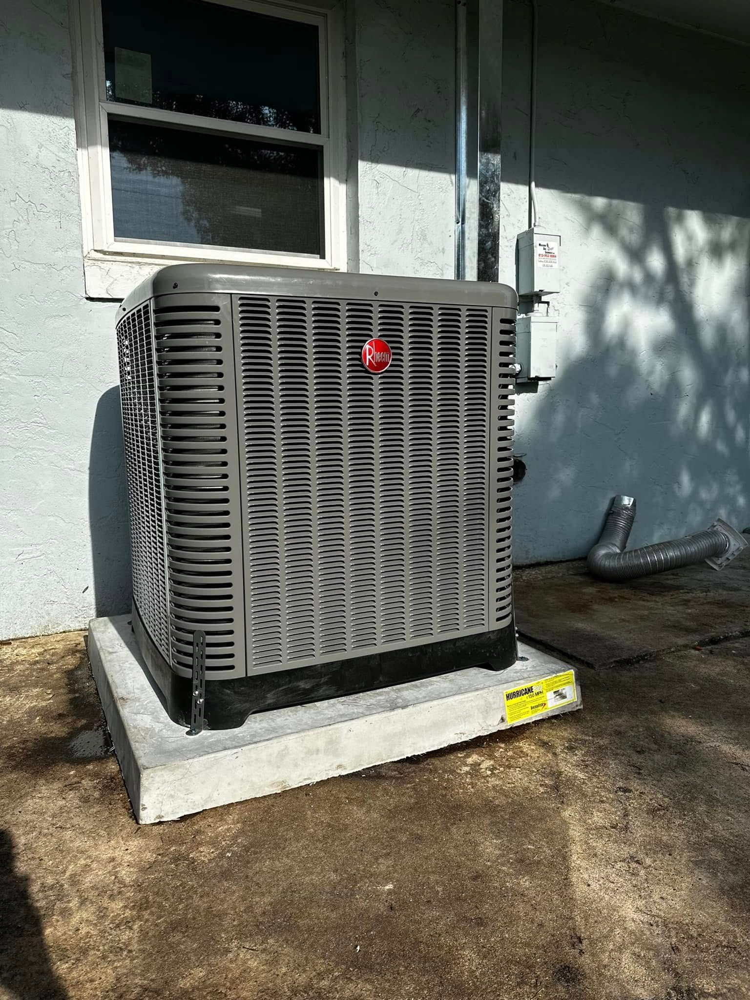 Gray outdoor HVAC unit beside a house wall and window on a concrete pad, with a yellow warning label.