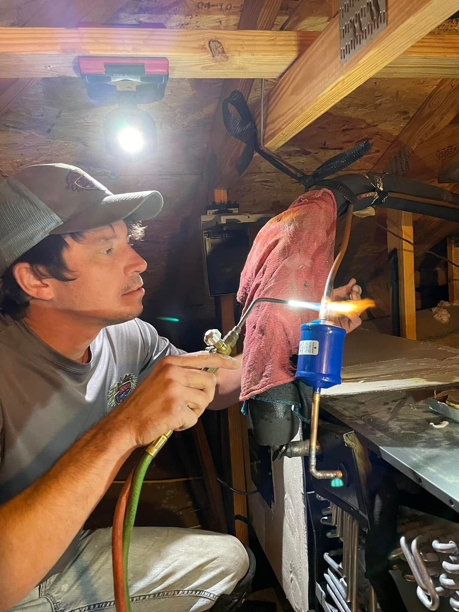 Worker using a handheld tool to repair a metal object in a cluttered workshop under a bright light