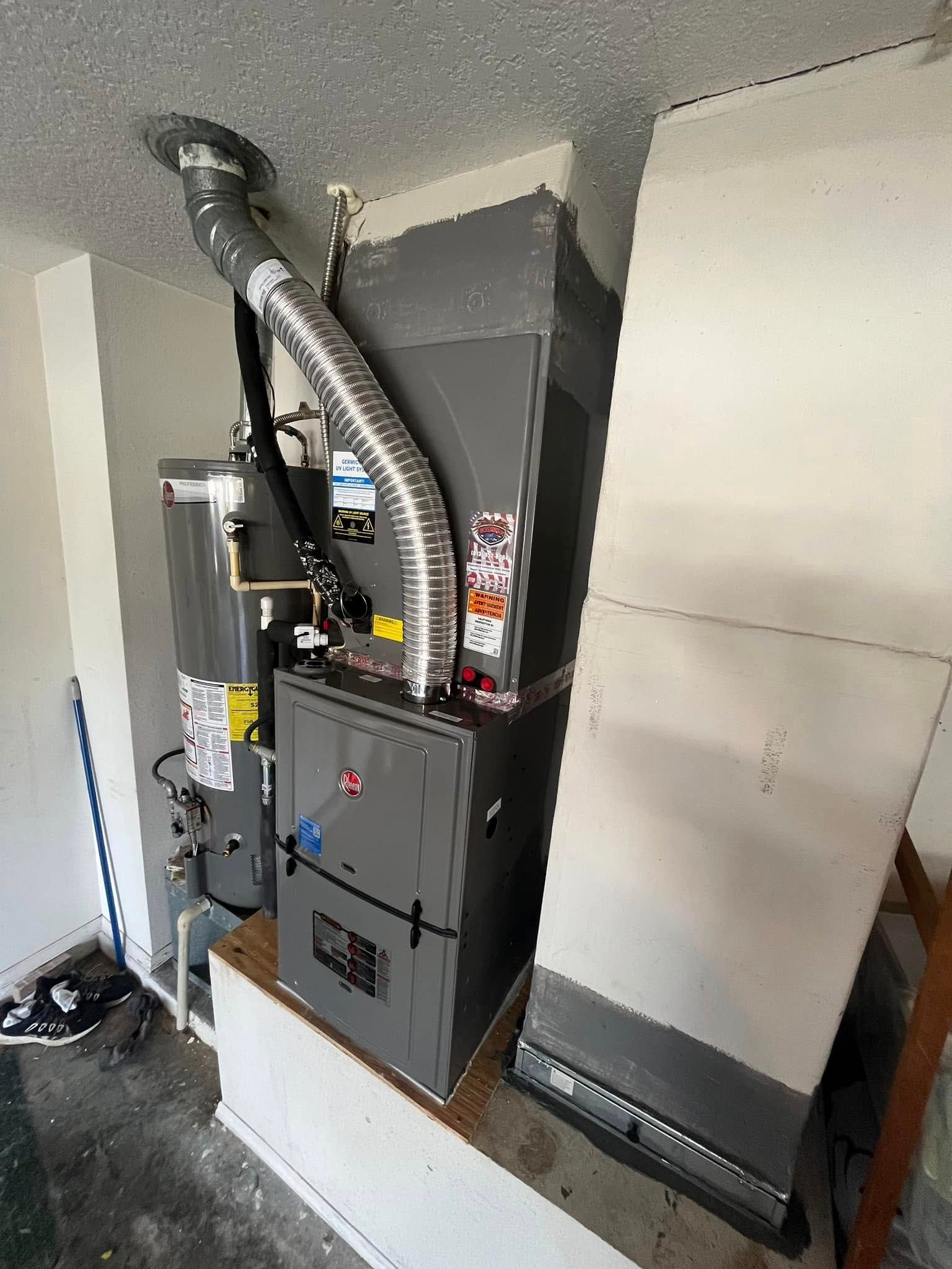 Large HVAC furnace and ductwork installed in a utility room, with metal vent piping and equipment panels.