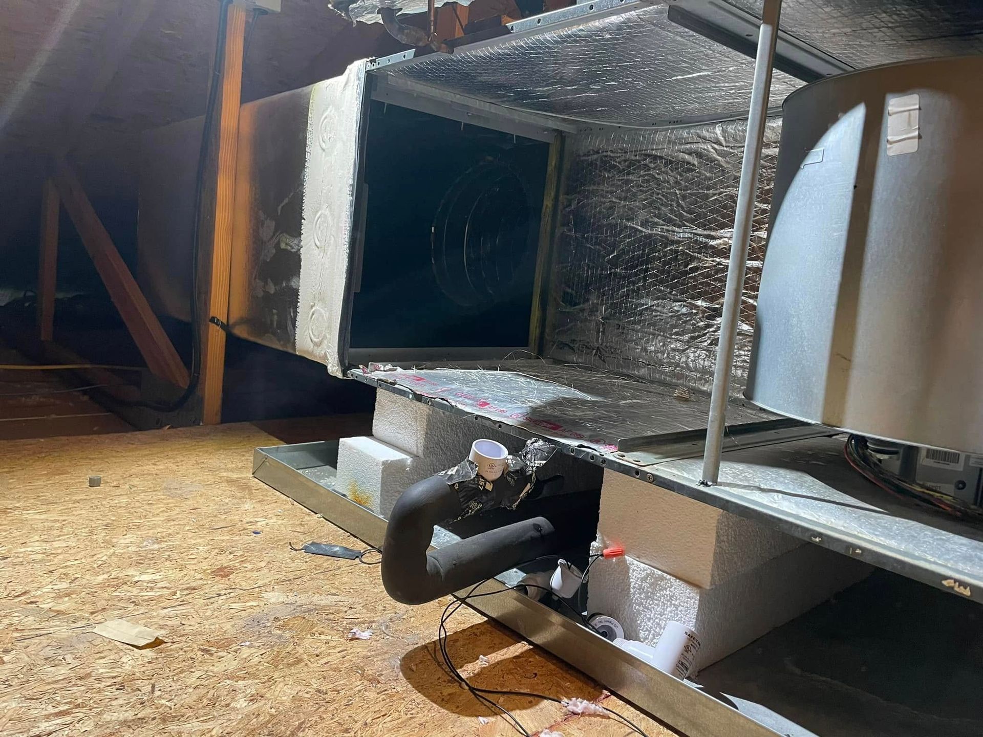 Insulated HVAC duct in an attic, with a black pipe and metal vent components on the floor