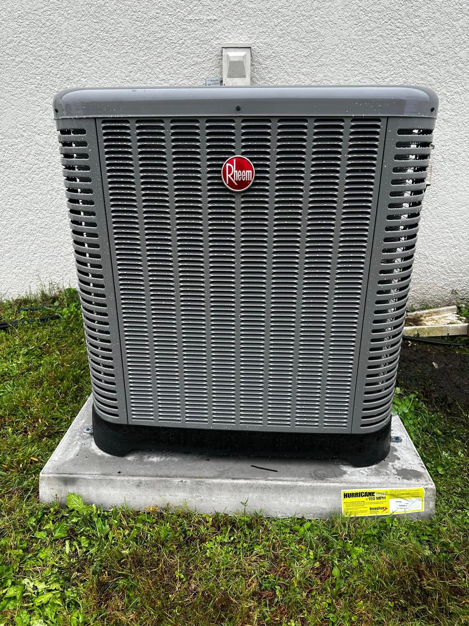 Outdoor HVAC unit with dark grille on a concrete pad beside a wall and grass.