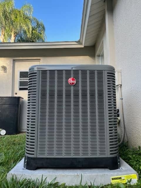 Outdoor HVAC unit beside a house, gray and black with a red logo, on a concrete pad