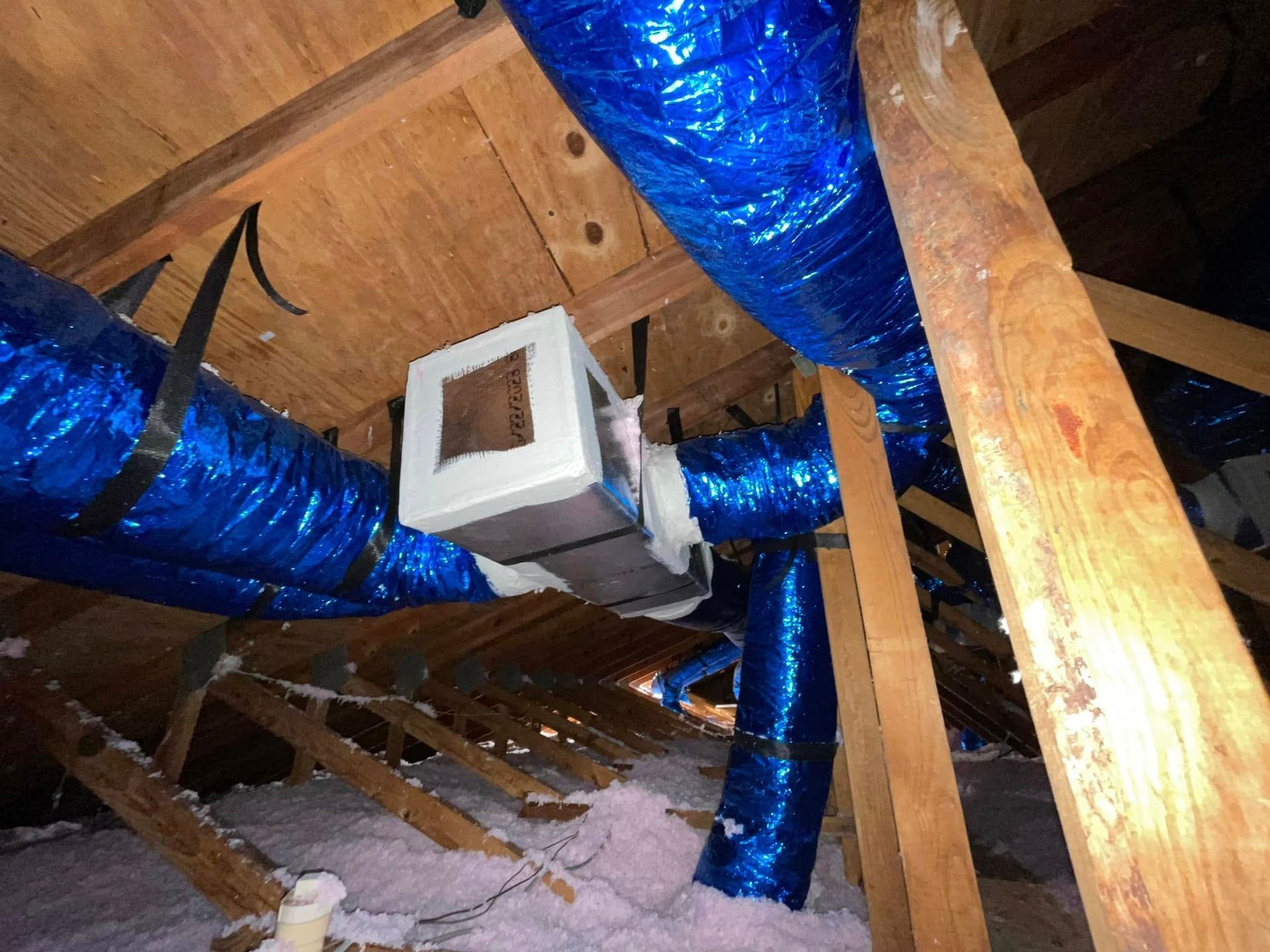 Attic with blue insulated ducts and exposed wooden rafters, plus a small vent or HVAC unit.