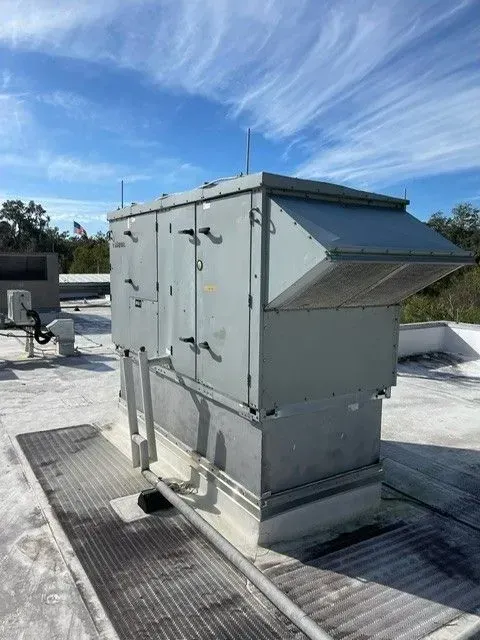 Gray rooftop HVAC unit with vented hood on a metal platform under a blue sky