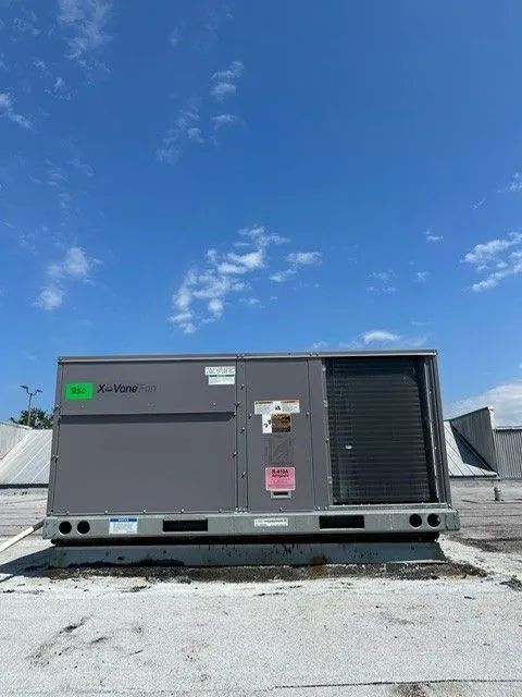 Gray rooftop HVAC unit under a bright blue sky on a gravel-covered roof.