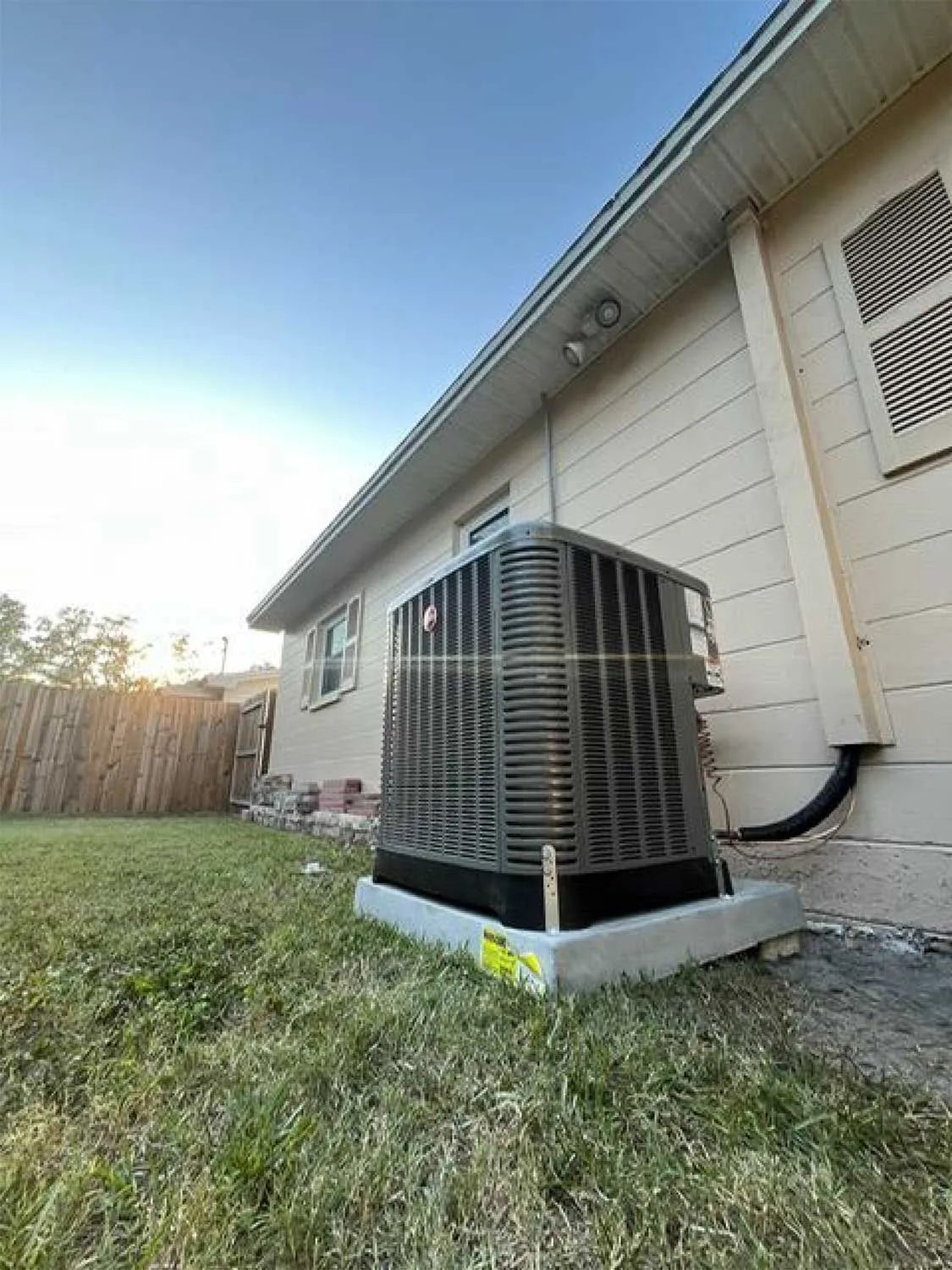 Outdoor air conditioner unit beside a beige house on a grassy lawn at sunset