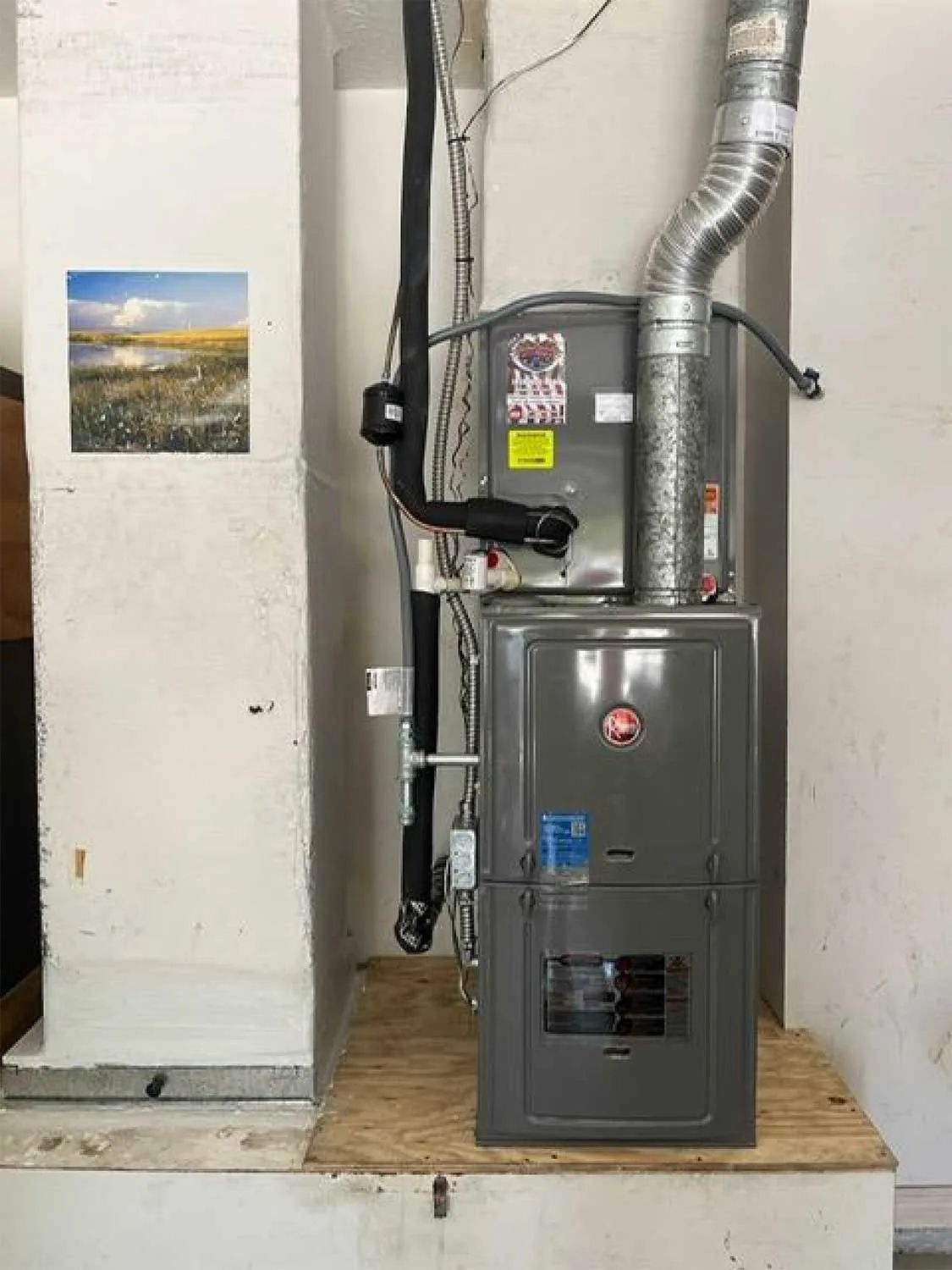 Furnace and water heater beside a wall, with silver vent pipes in a small utility room.