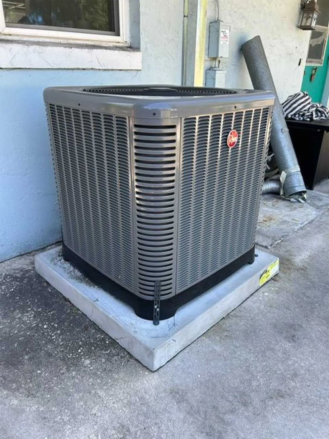 Outdoor air conditioner unit beside a building wall, on a concrete pad.