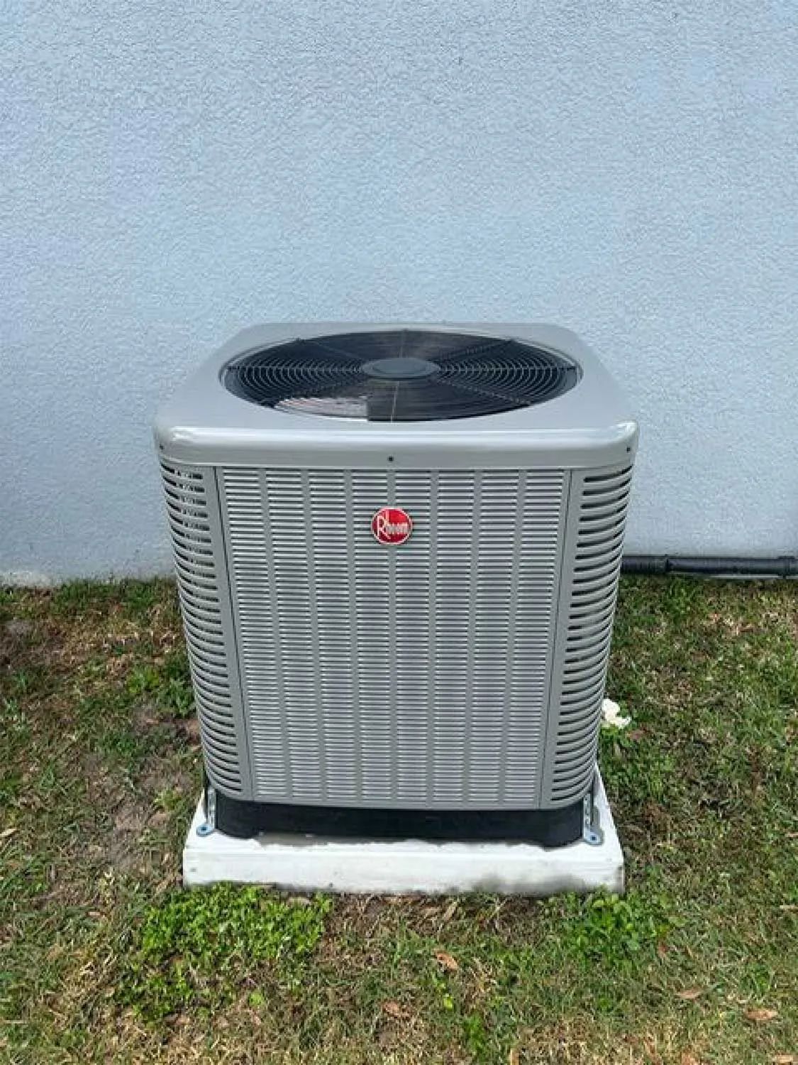Outdoor HVAC condenser unit against a white wall on grass.