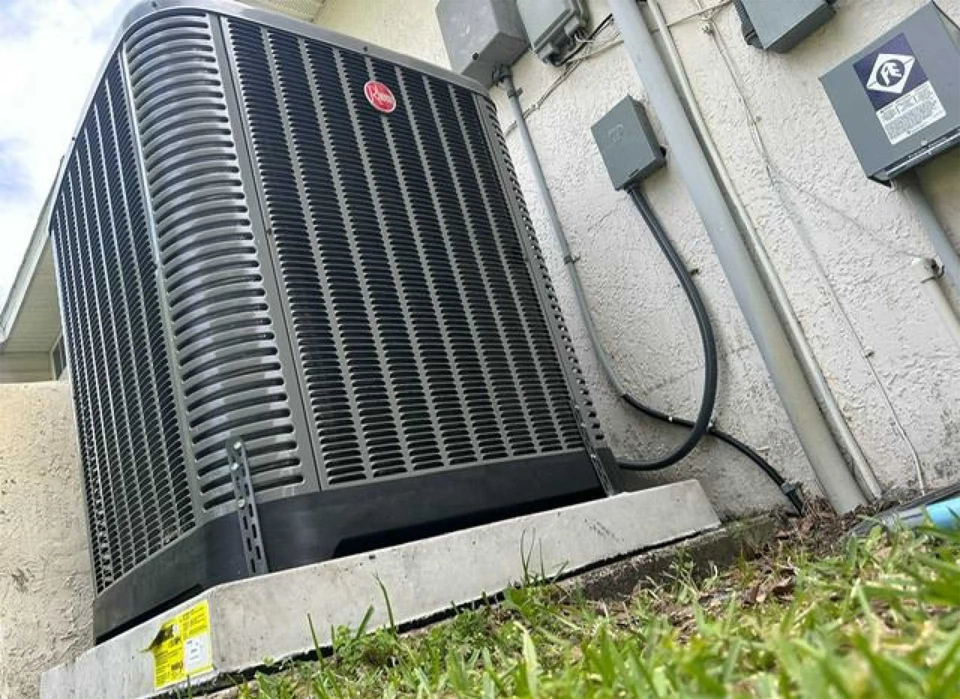 Outdoor air conditioner condenser unit beside a building wall with visible wiring
