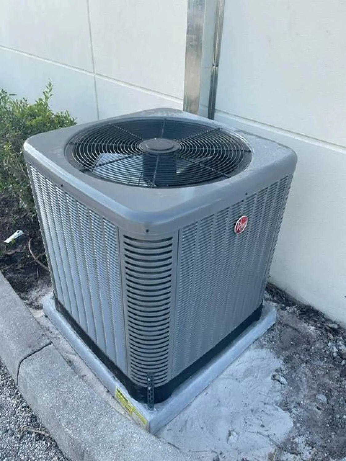Outdoor air conditioning unit beside a wall, with a fan on top and gray siding.