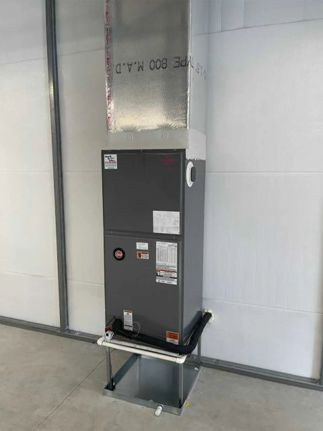 Commercial HVAC unit mounted on a wall in a tiled utility room with metal ductwork above.