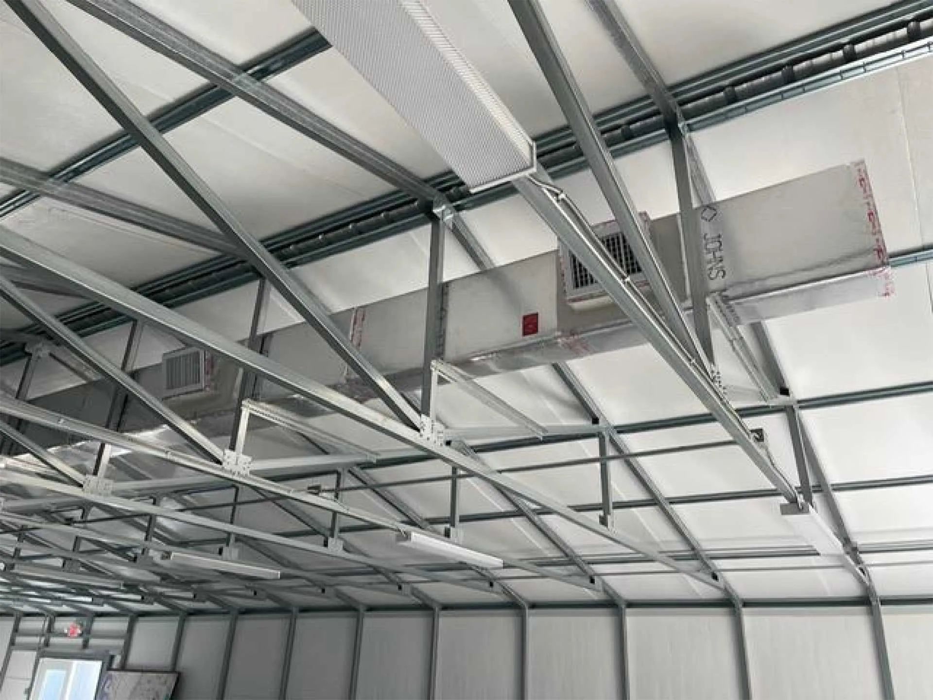 Interior of a steel-framed warehouse roof with ducts, vents, and insulation panels overhead