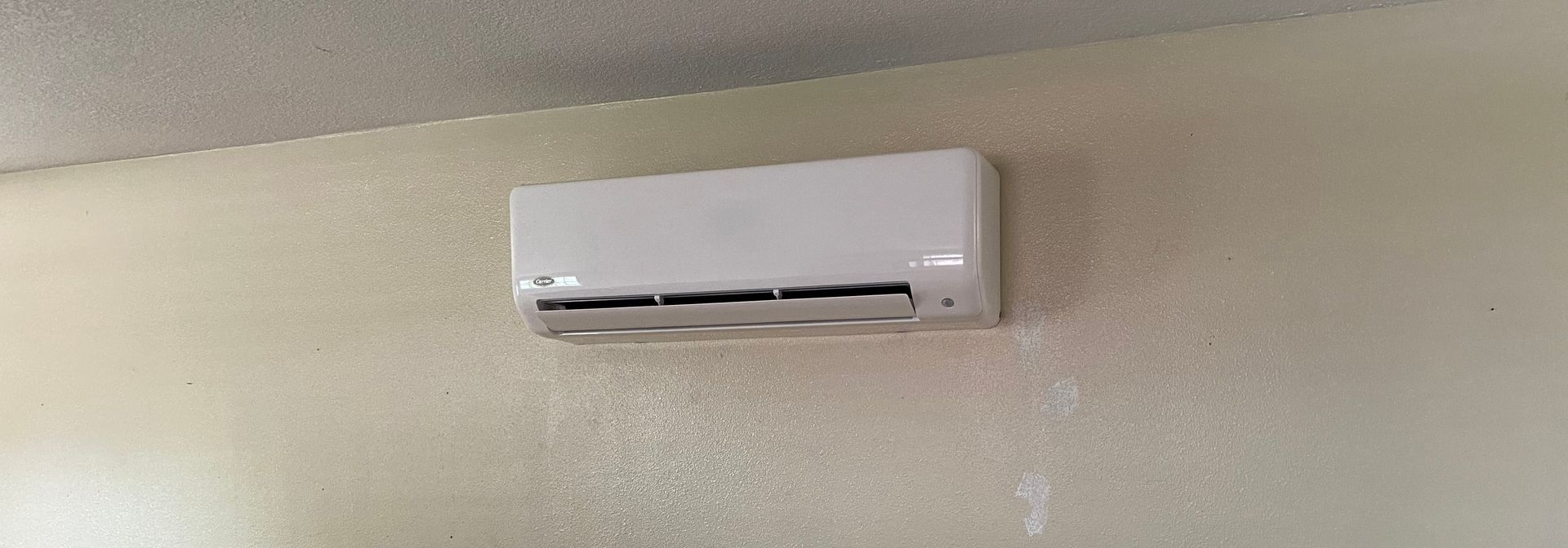 Wall-mounted white air conditioner on a beige wall in a room.