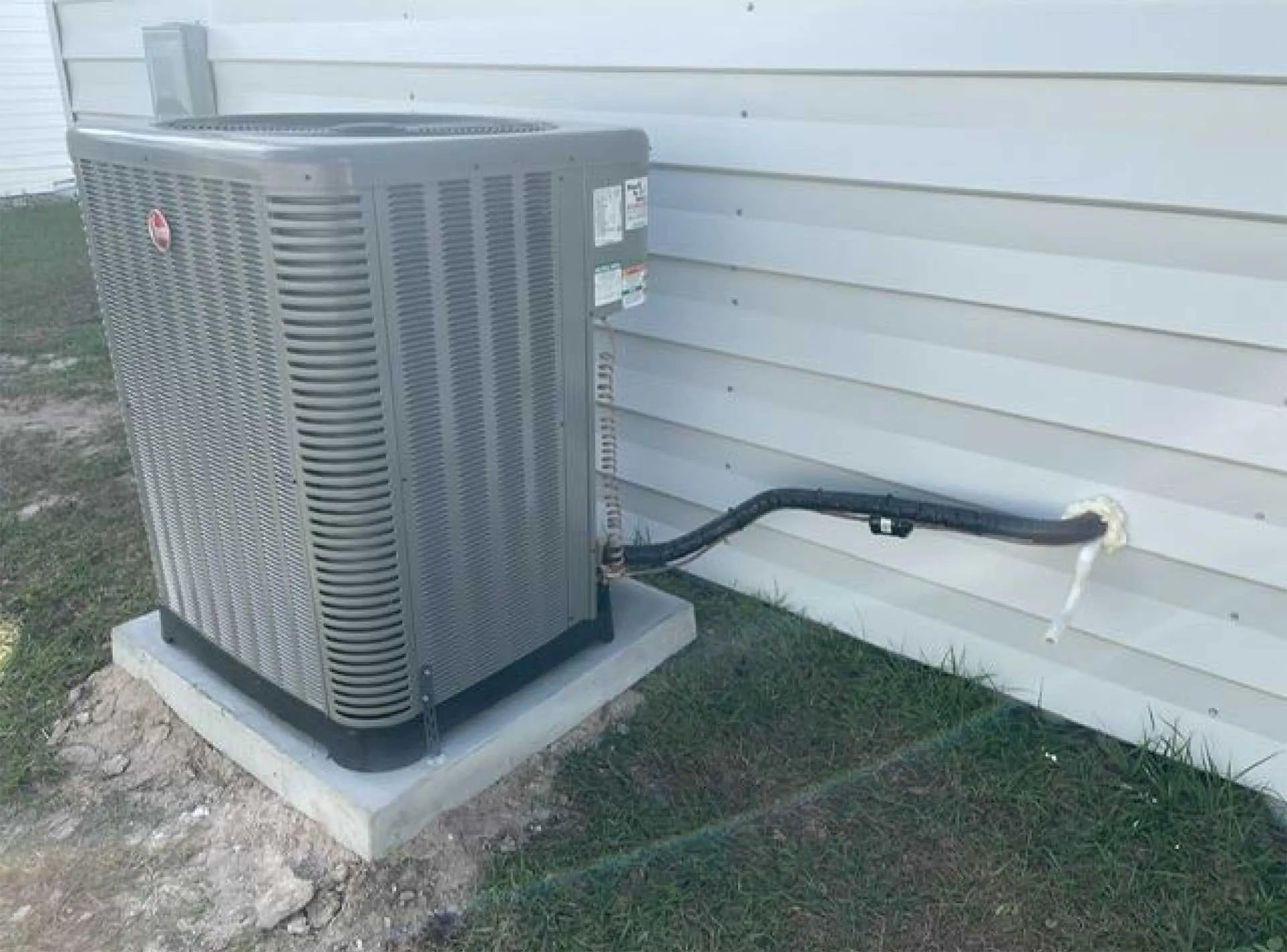 Outdoor air conditioner unit beside a house, connected by insulated refrigerant lines.