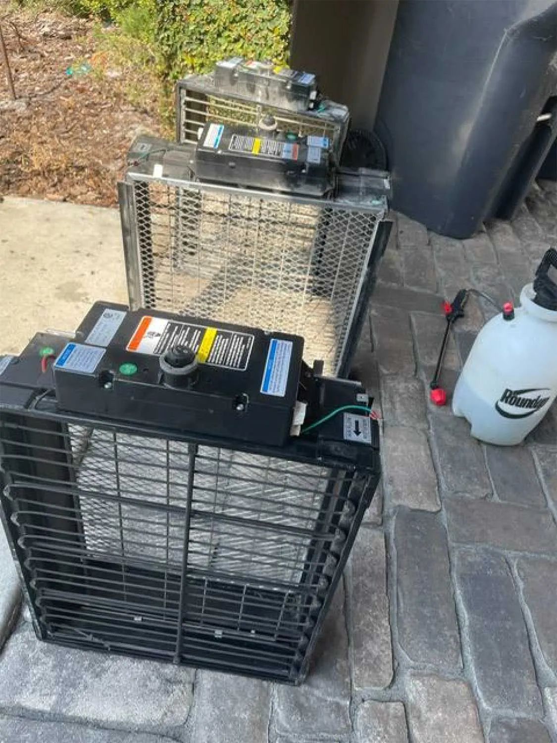 Two large battery packs on plastic crates beside a paved driveway and a white spray bottle