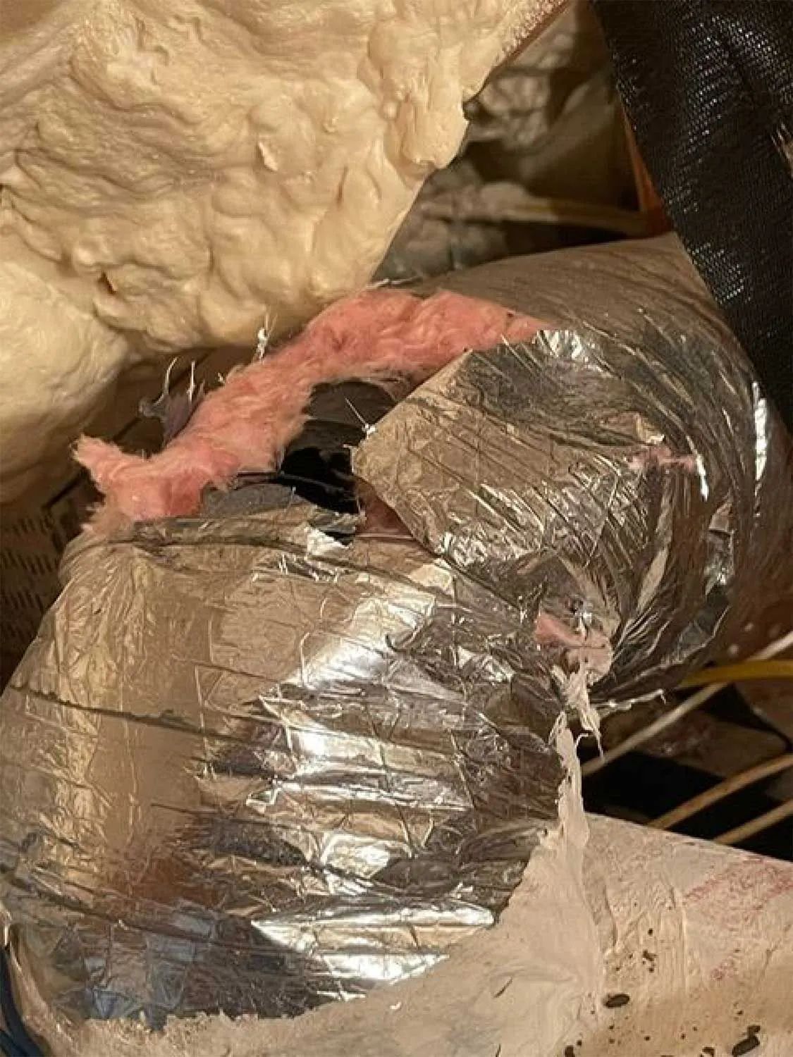 Insulated HVAC duct with torn silver foil and exposed pink fiberglass insulation
