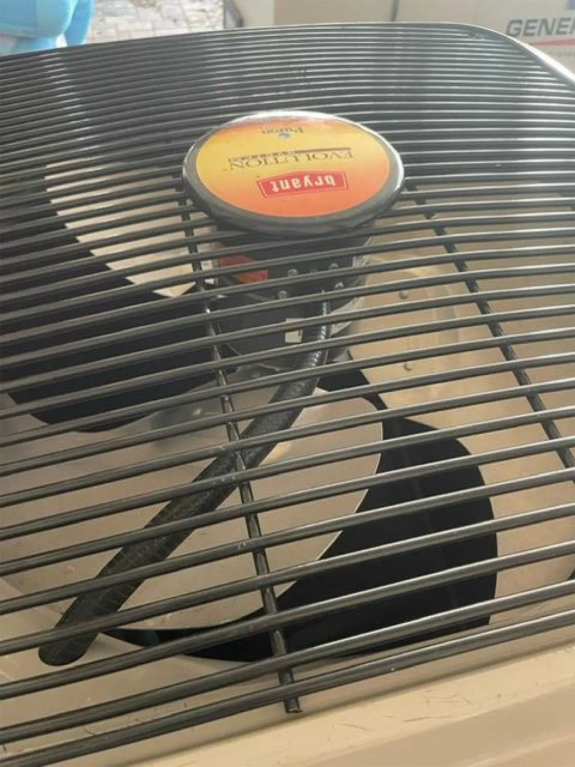 Close-up of a dusty window fan with black blades and a yellow-orange center label