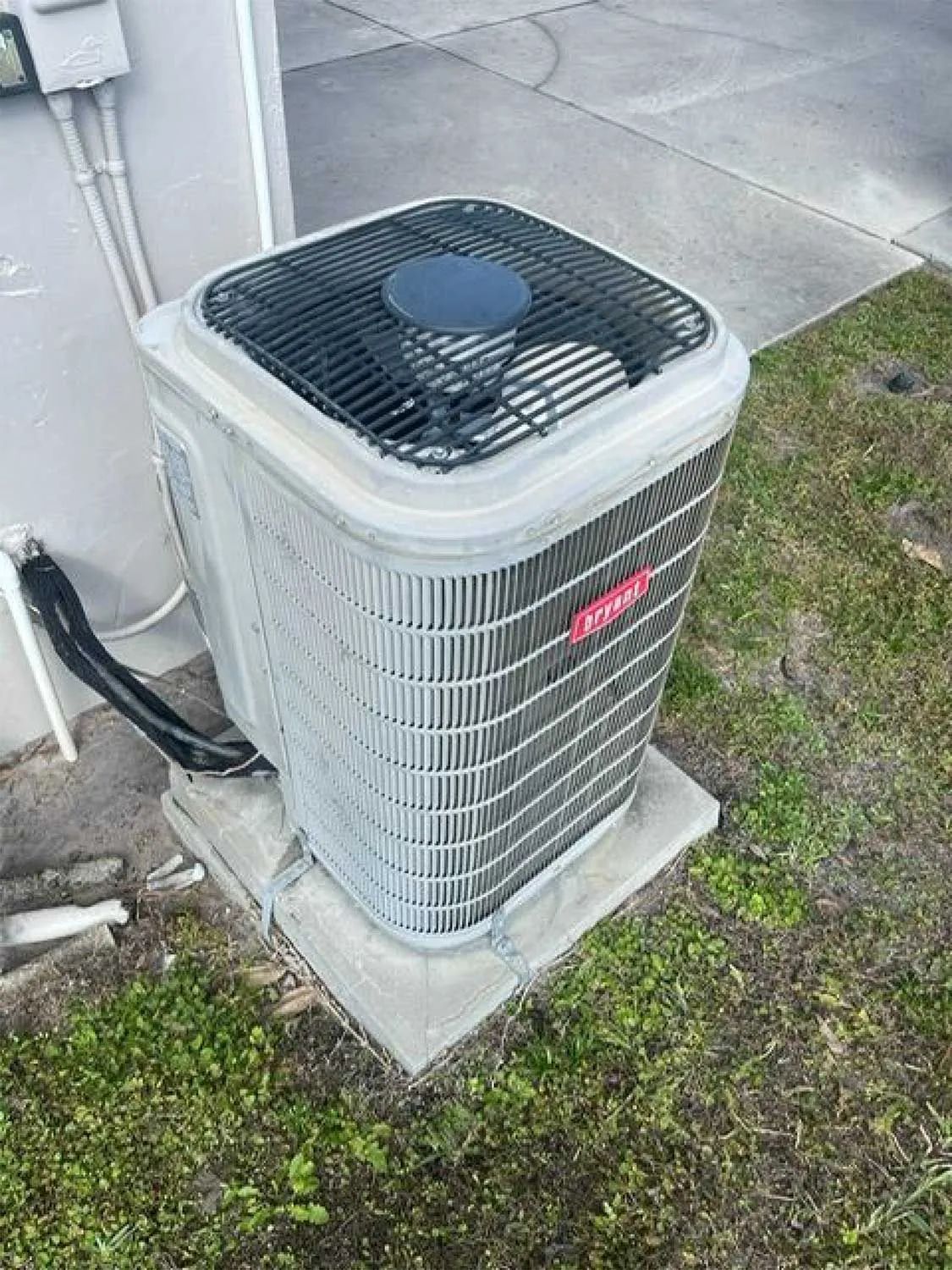 Outdoor central air conditioner unit beside a house, with grass and concrete pad nearby.
