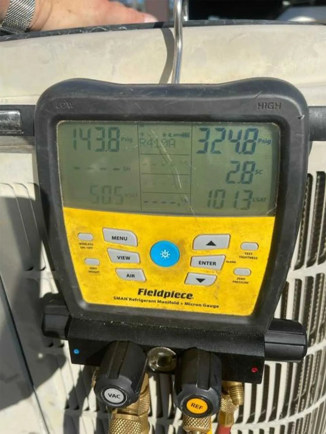 Fieldpiece HVAC gauge with digital readings and yellow control buttons on a work surface