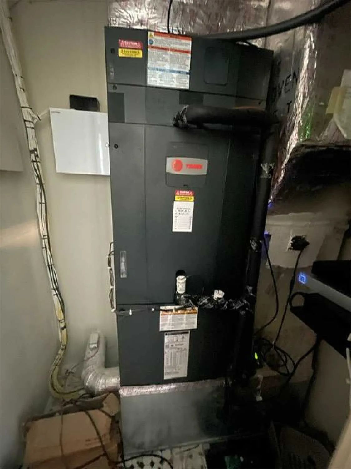 Black HVAC furnace in a basement utility space with exposed ductwork and pipes
