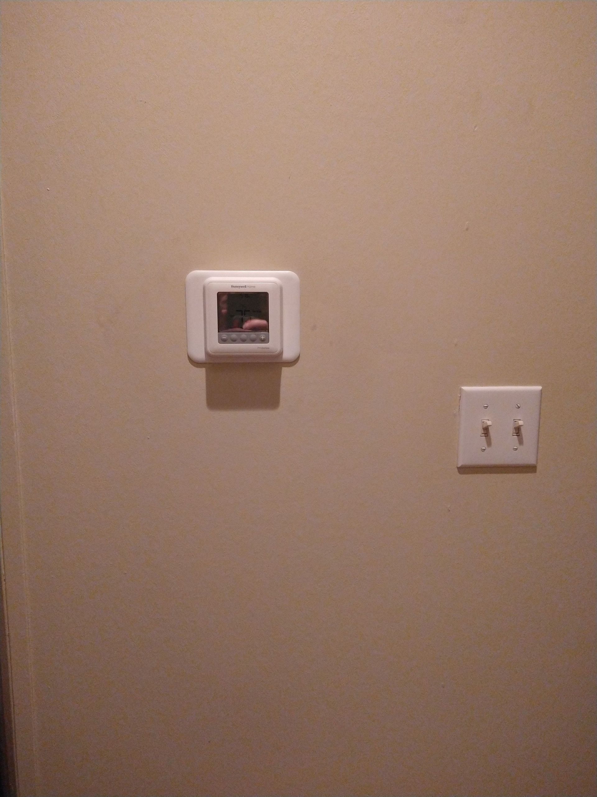 Beige wall with a small thermostat and a double light switch panel.