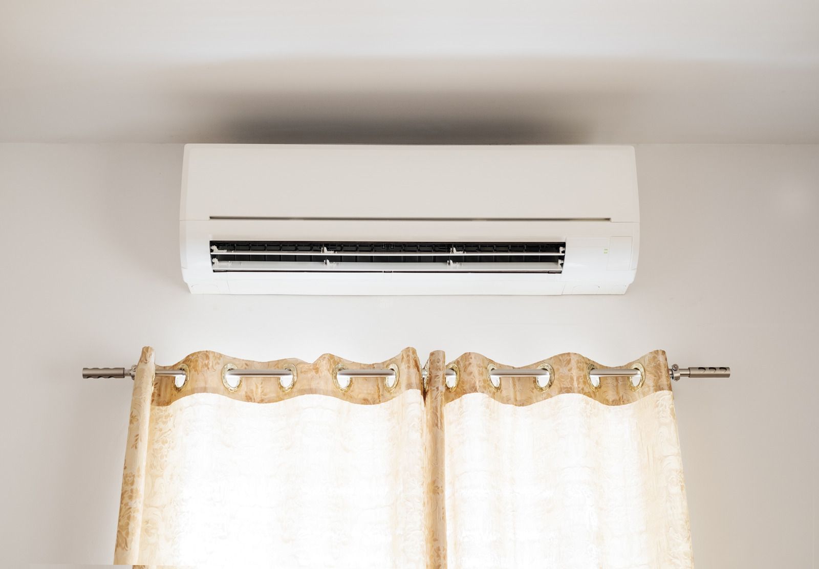 White wall-mounted air conditioner above a window with sheer curtains and decorative curtain rod