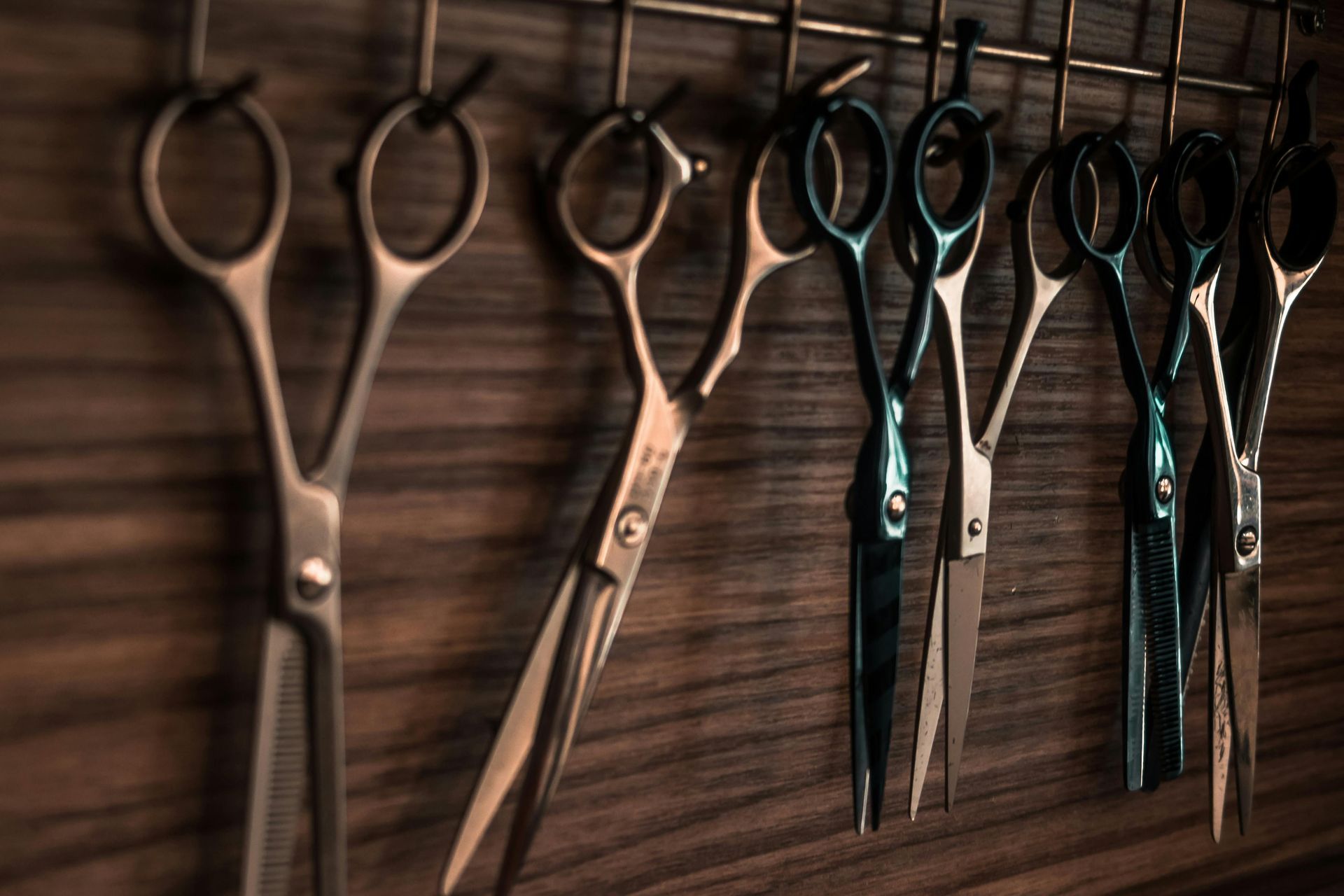 Several hairdressing scissors hanging on a wooden wall rack