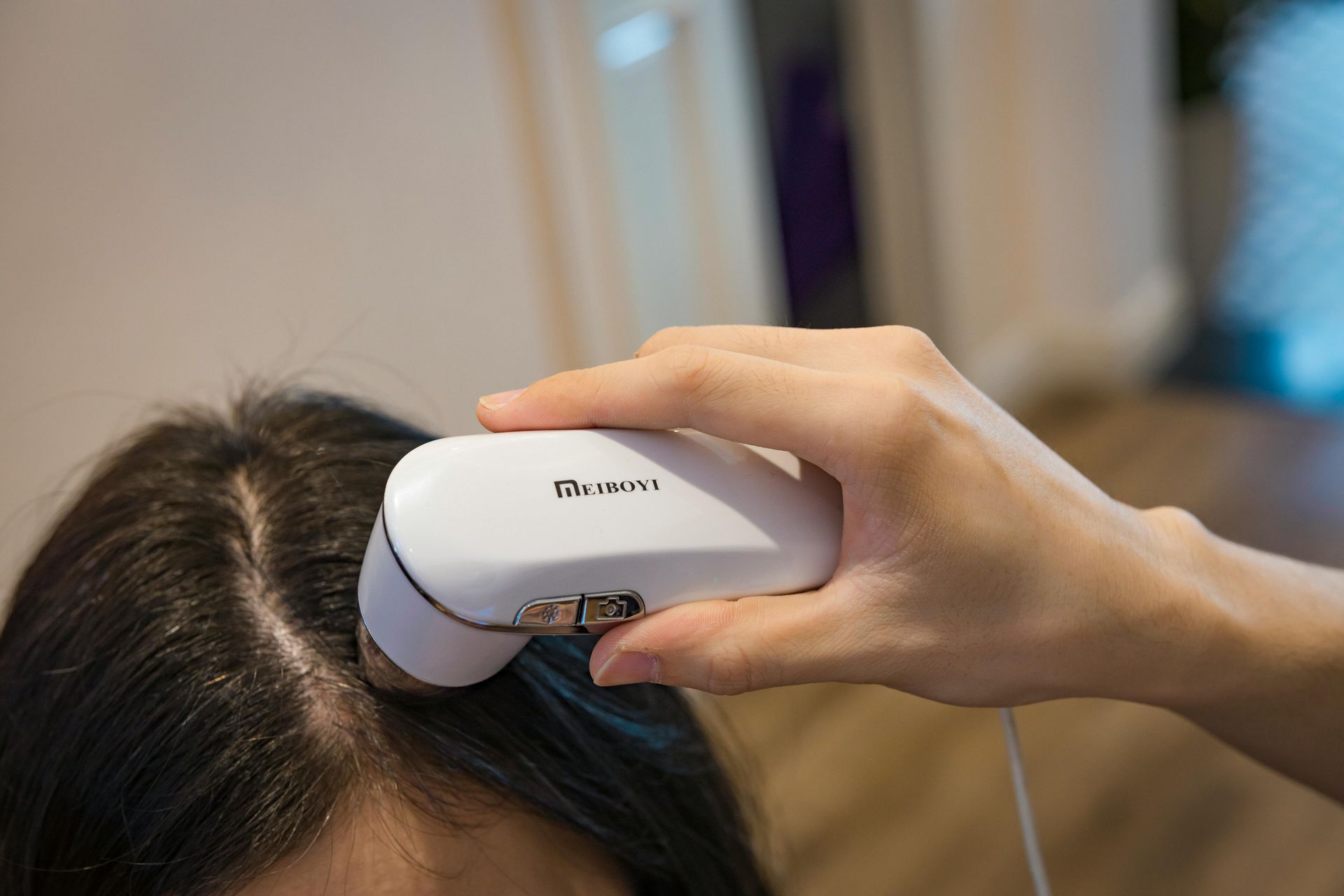 Hand holding a white handheld device against a person’s dark hair near the scalp