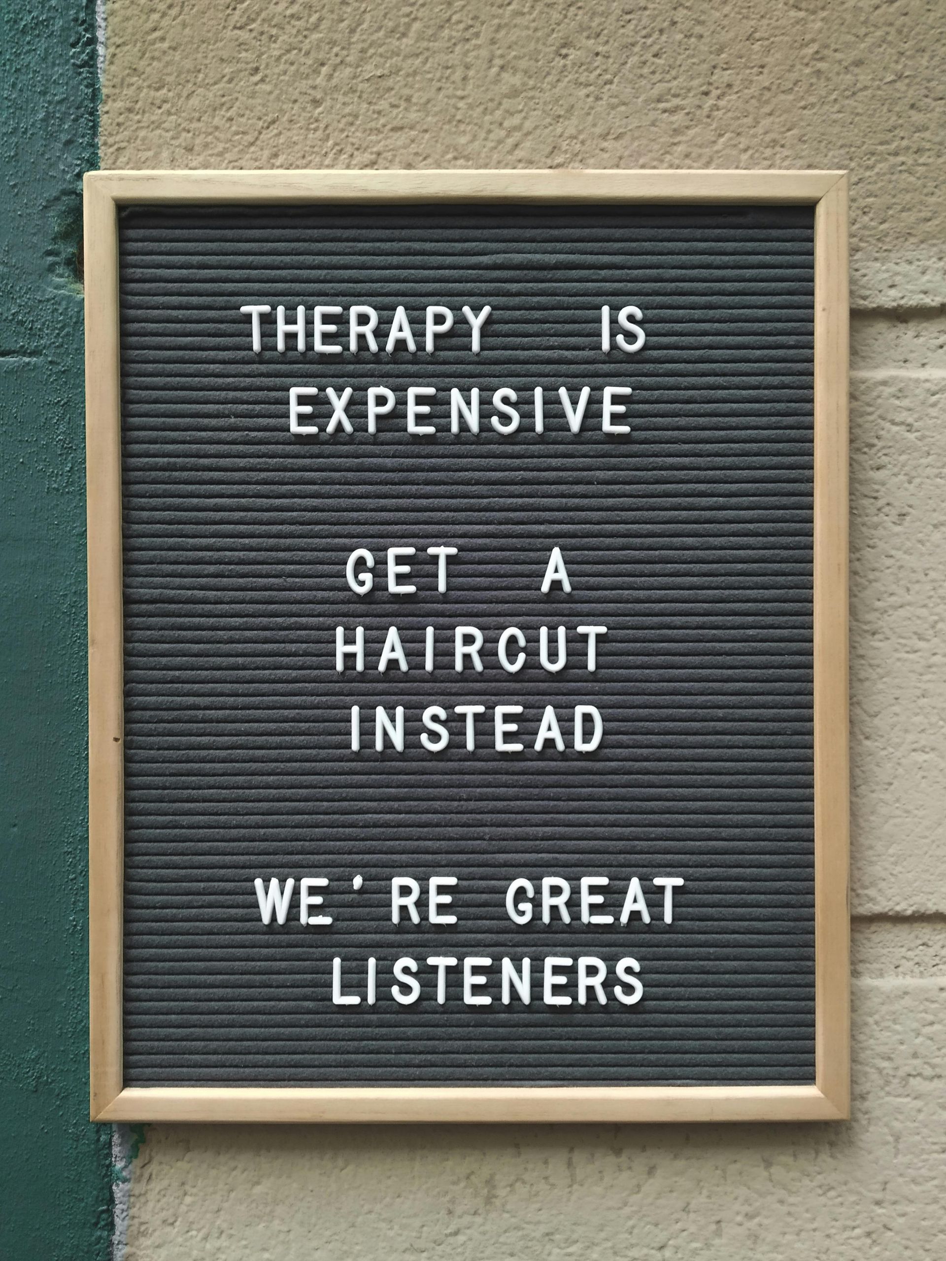 Black letter board with white text: “Therapy is expensive. Get a haircut instead. We’re great listeners.”