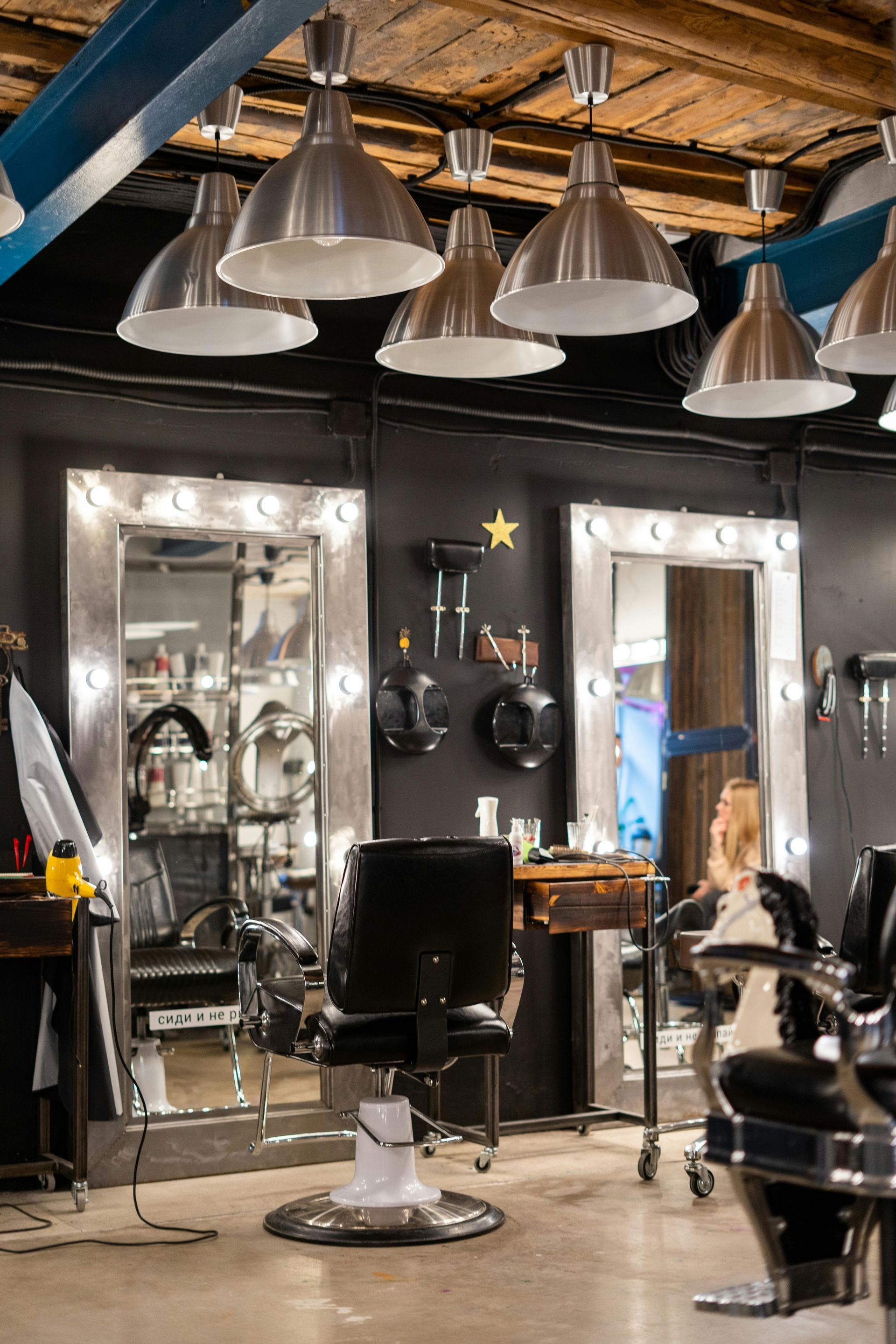 Modern barber shop with black chairs, mirrors, and silver pendant lights under an exposed wooden ceiling