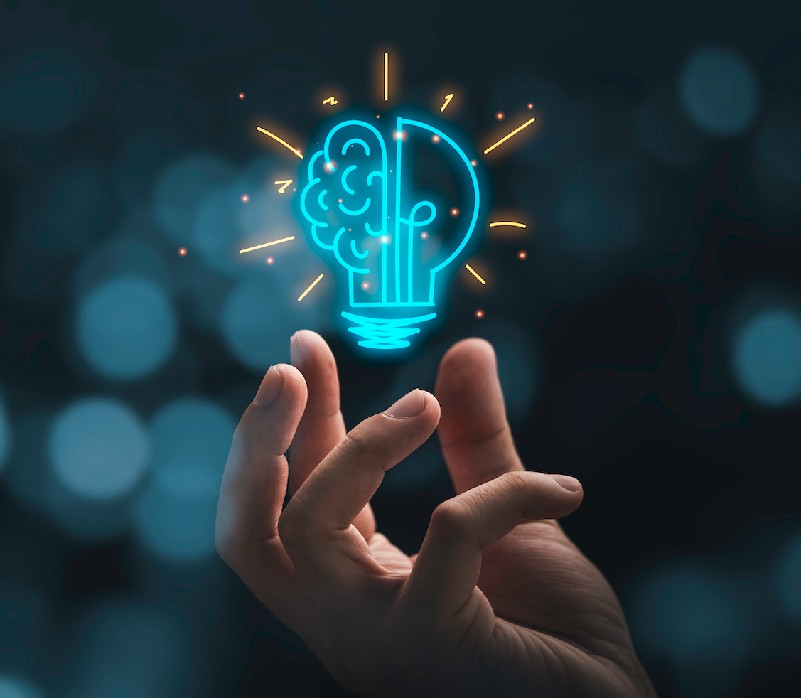 Picture of a hand with the blue outline of a lightbulb hovering above it. The lightbulb outline is split into two: on one side is the outline of a lightbulb, on the other side is the outline of a brain.