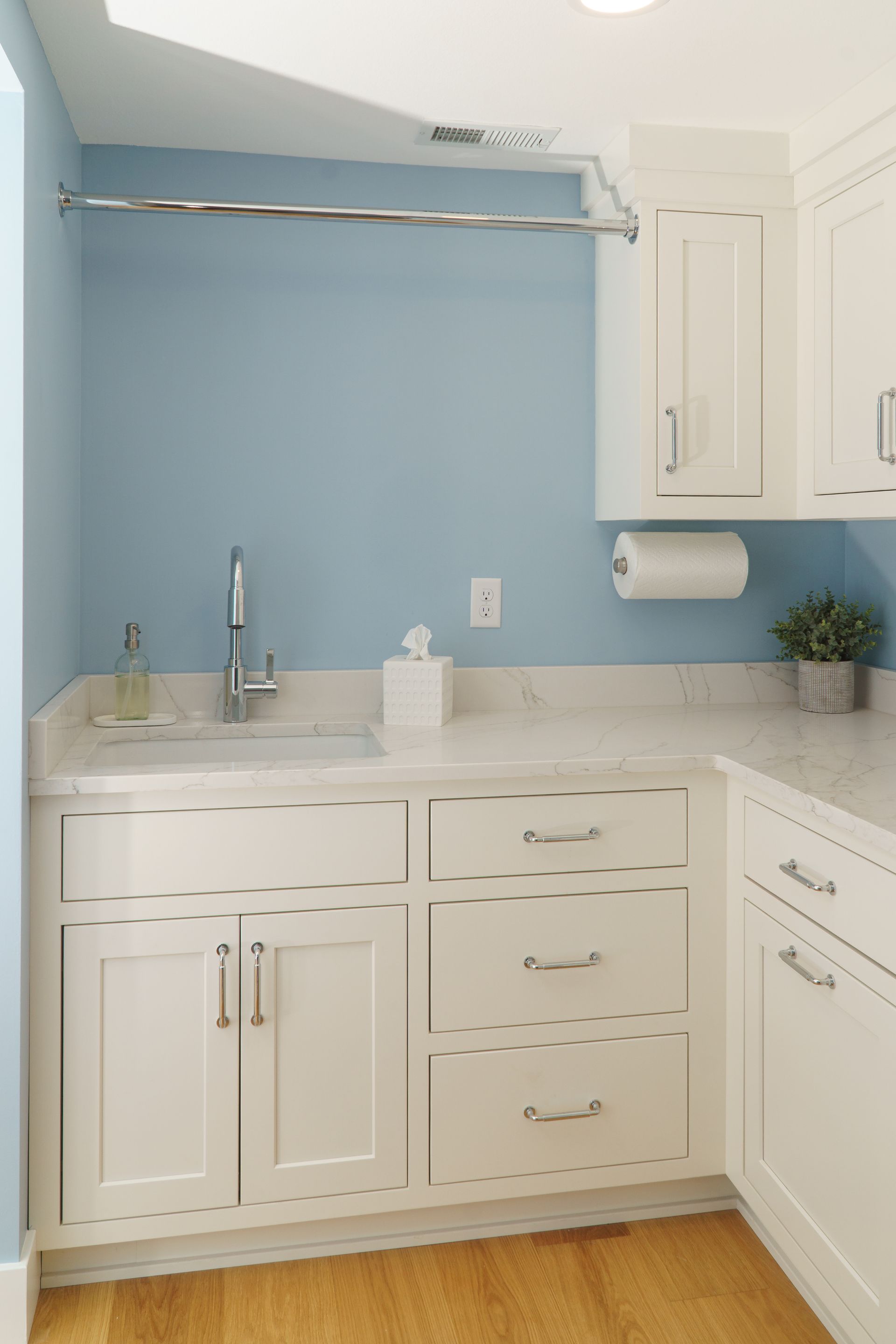 Custom white painted wood laundry cabinets with inset doors and drawers and clothing rod.