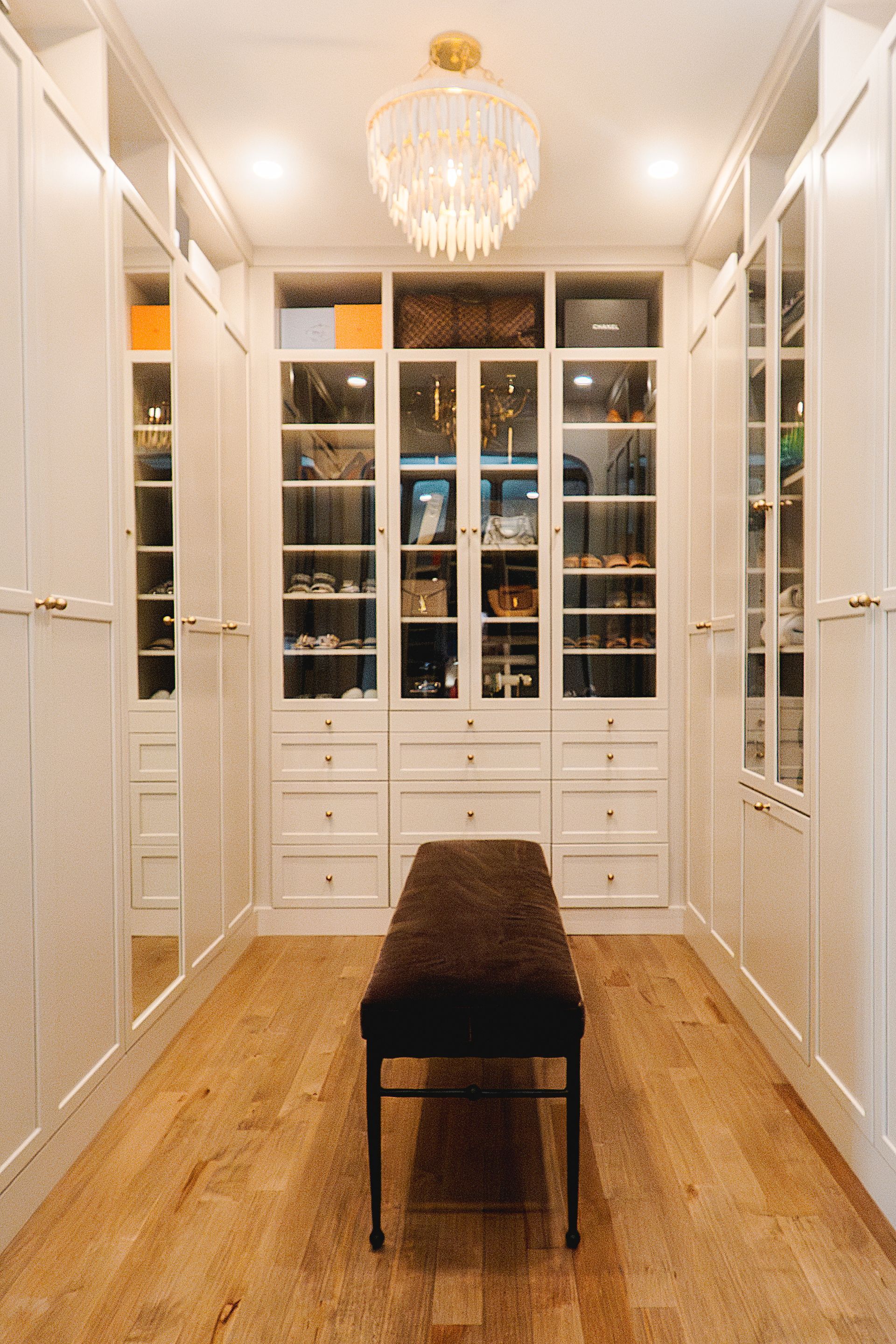 Custom white painted wood closet storage solution with glass doors and chandelier.
