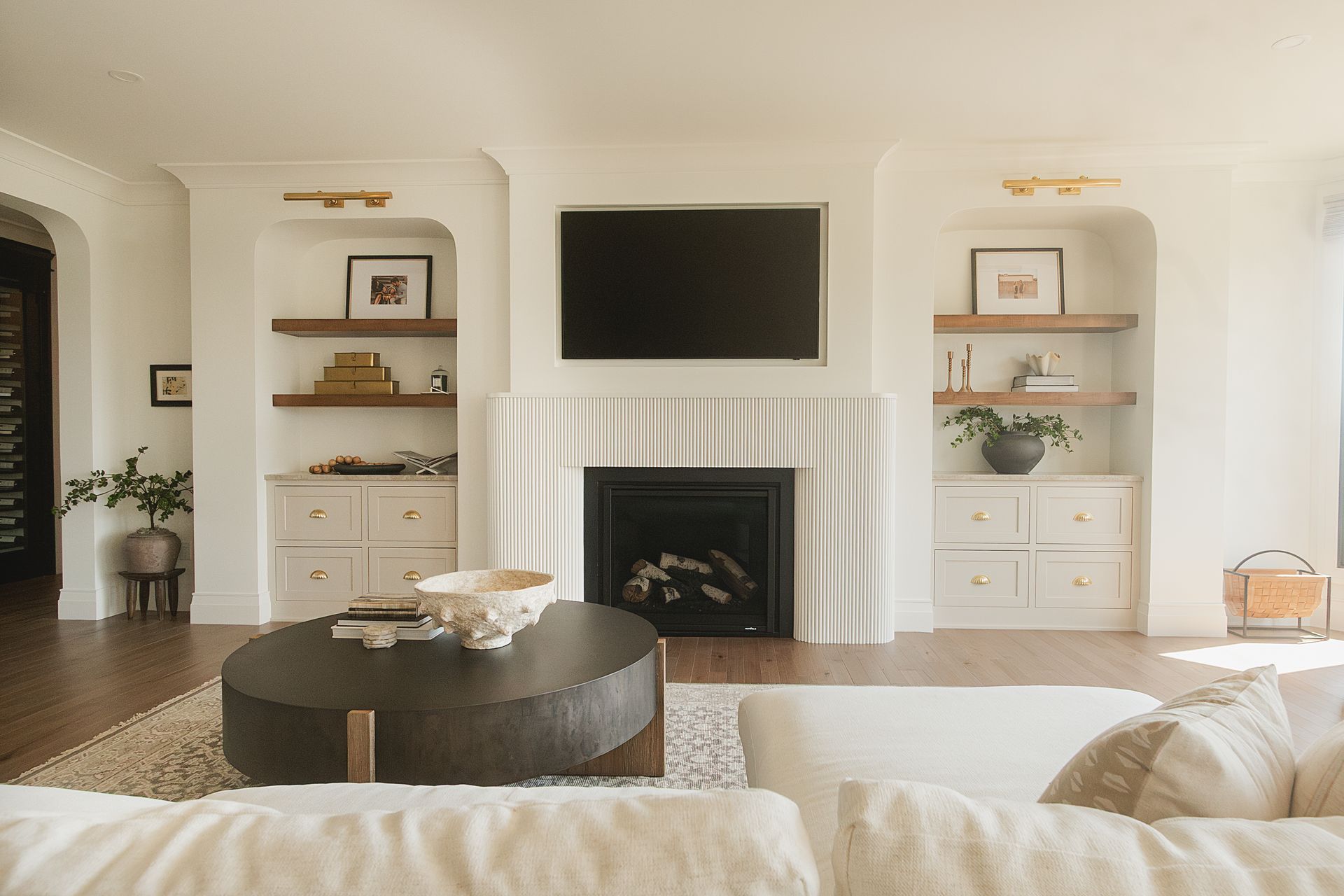 Custom white painted wood cabinet and stained floating shelves with arched opening by fireplace.