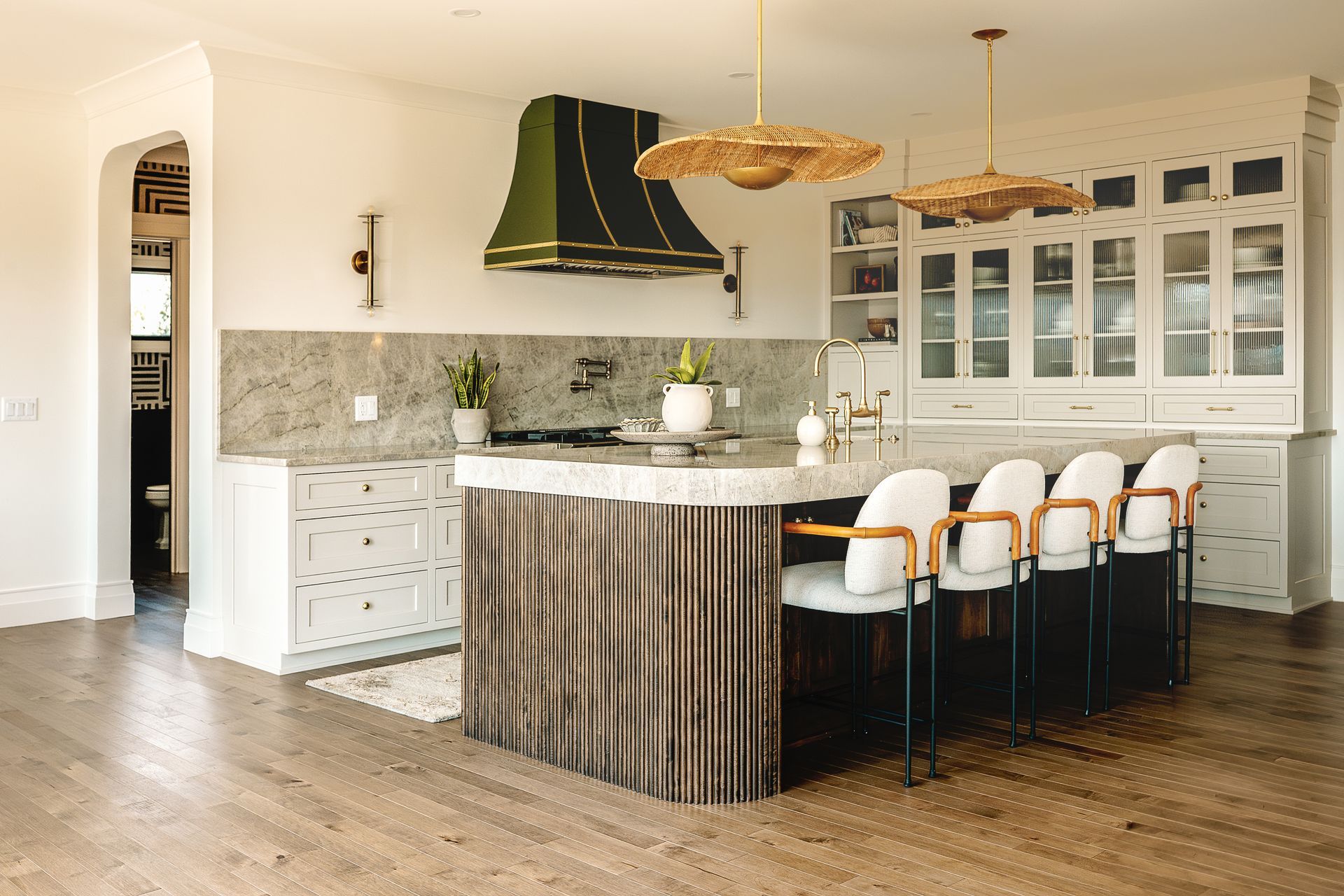 Custom white painted kitchen cabinets and unique reeded curved island and custom green range hood with reed pendant lights.