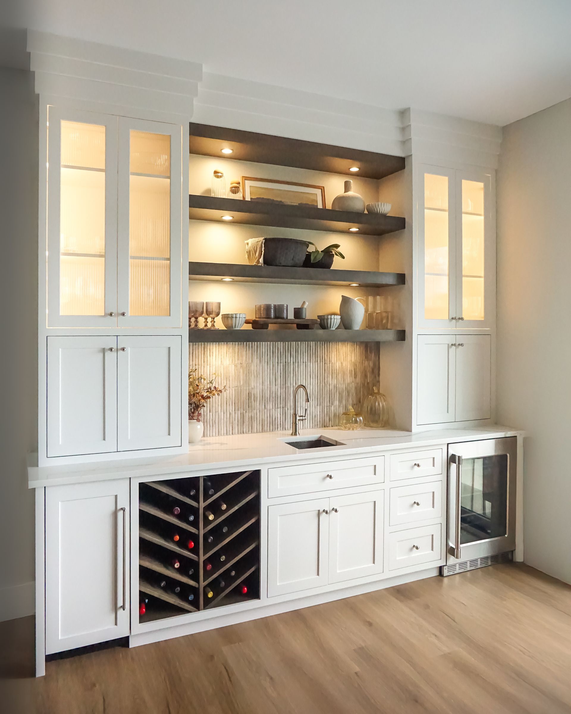 Custom white painted wood beverage center with floating stained wood shelves and in-cabinet lighting.