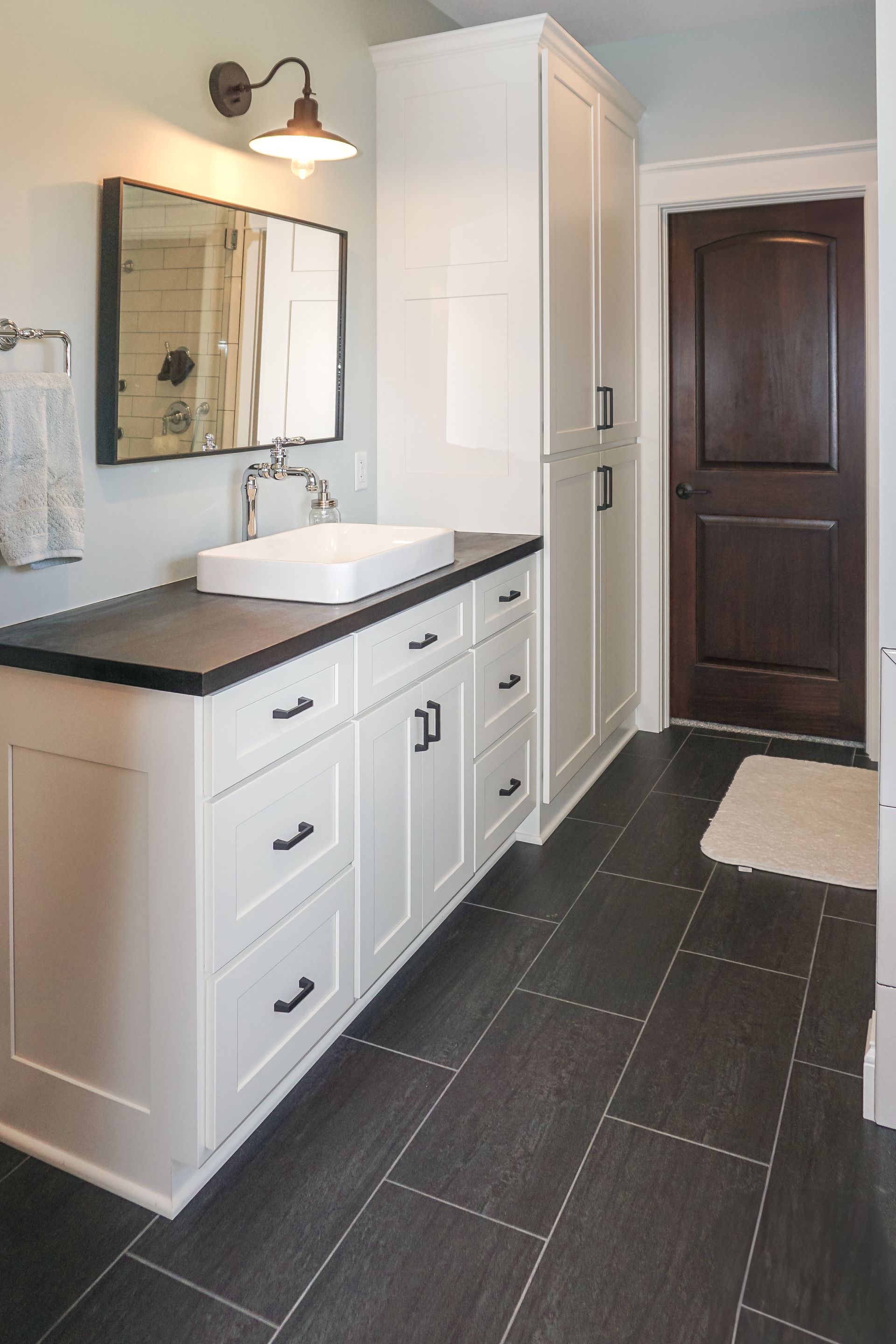 Custom white painted wood bathroom vainity and linen closet with rectangular sink and dark floors.