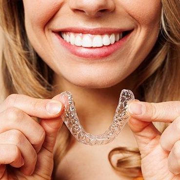 Woman smiling and holding a clear dental aligner tray near her mouth