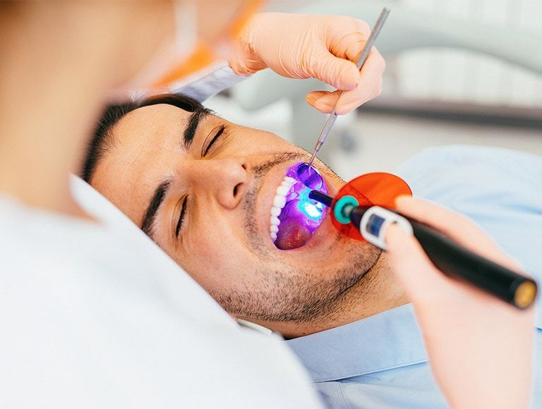 Dentist adjusting a woman’s teeth with pink gloves during a dental procedure