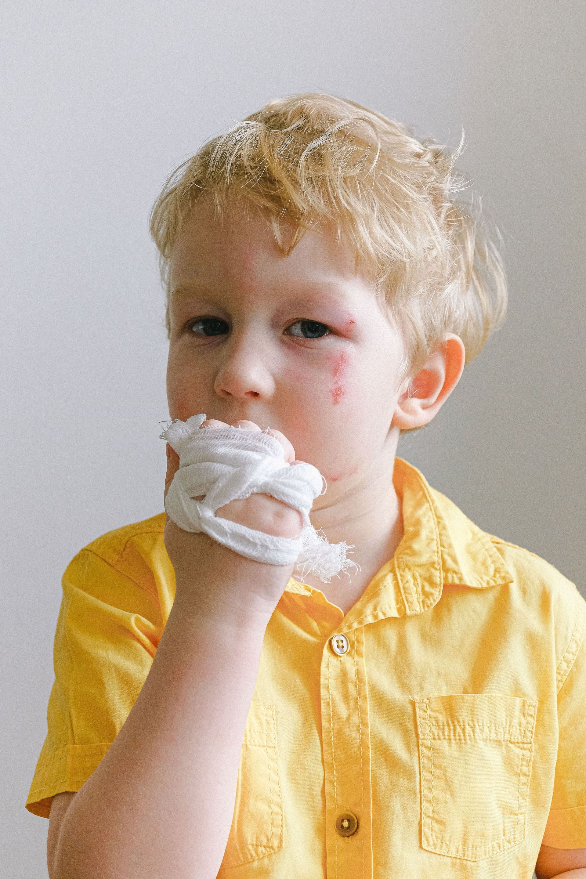 Child in a yellow shirt with soap suds on their hand and face, looking at the camera.