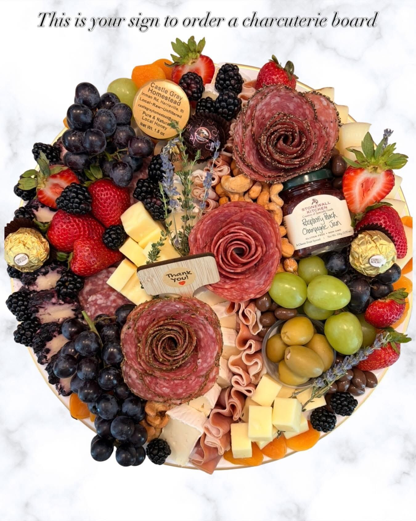 Heart-shaped charcuterie board with meats, cheeses, grapes, berries, olives, and crackers on a white surface