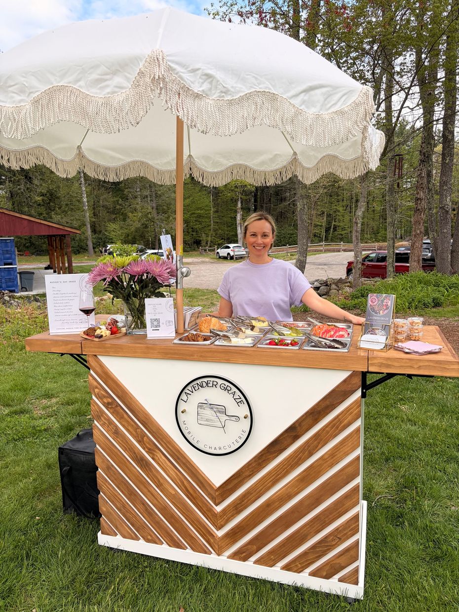 Outdoor dessert booth with a person behind a decorated table under a white umbrella, displaying pastries and flowers