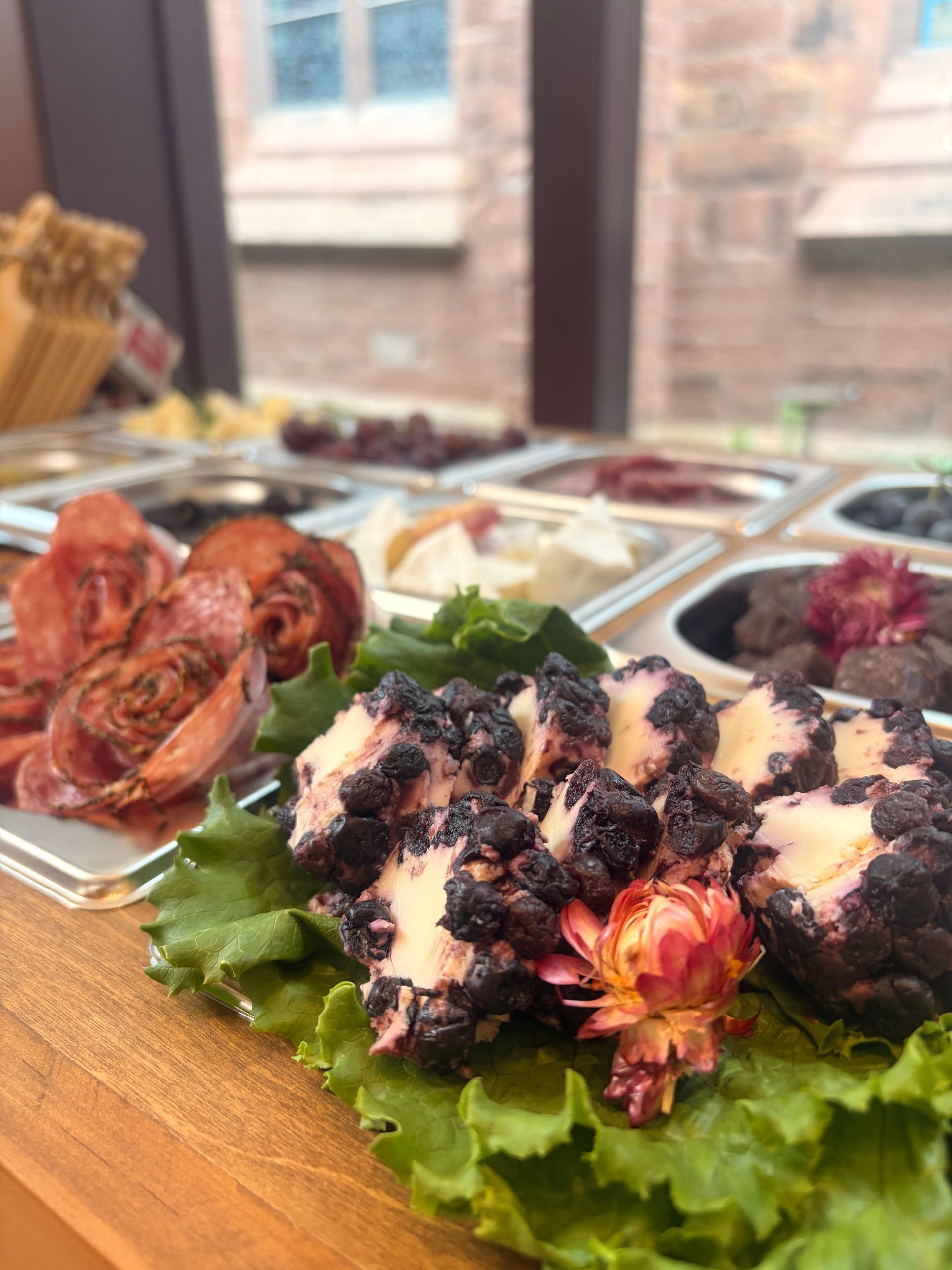 Charcuterie-style appetizers on a wooden board with greens and dark purple topping at a buffet table